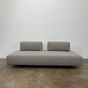 A minimalist gray Paola Lenti Orlando sofa bench from Modern Resale, featuring a 37" square design with one backrest and two rectangular cushions, is set against a plain white background.