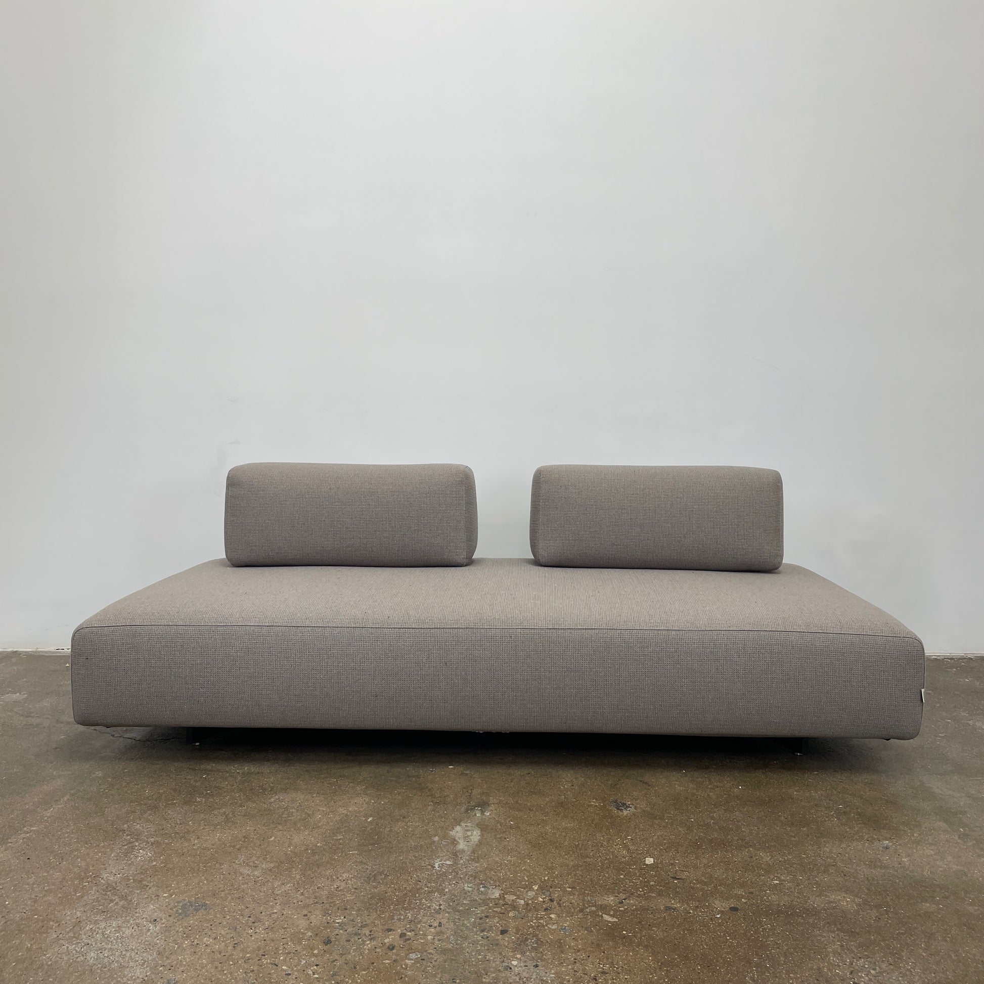 A minimalist gray Paola Lenti Orlando sofa bench from Modern Resale, featuring a 37" square design with one backrest and two rectangular cushions, is set against a plain white background.