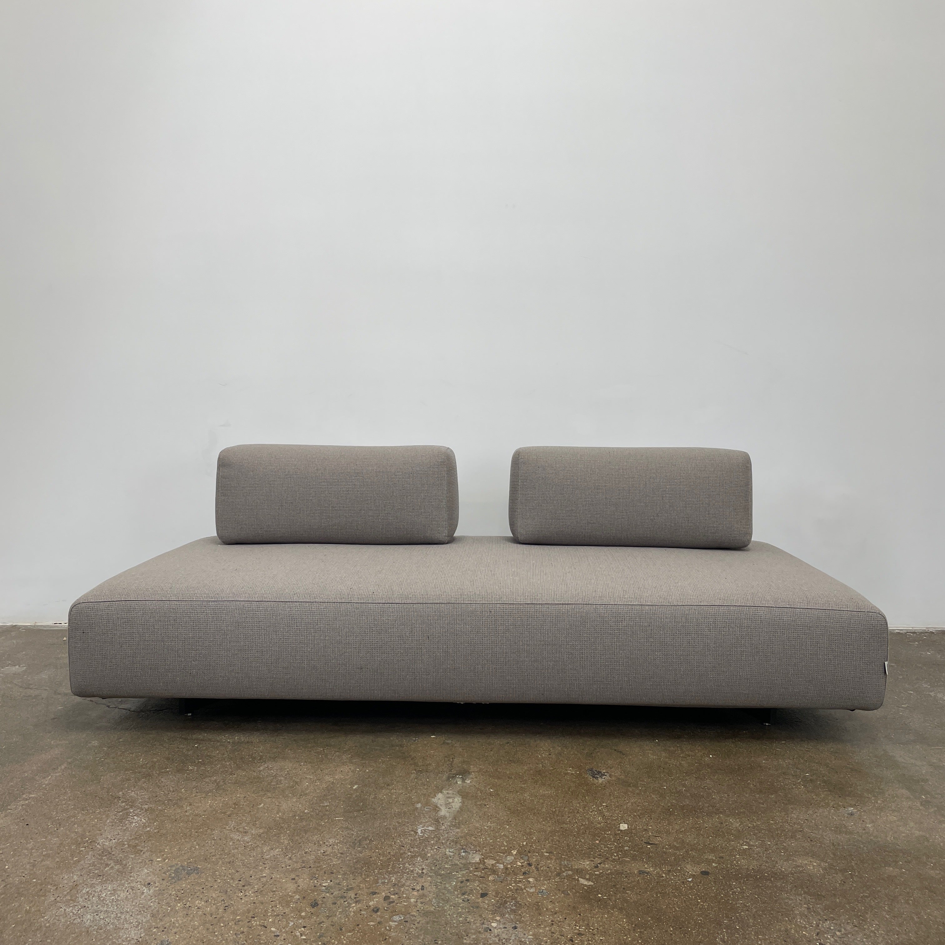 A minimalist gray Paola Lenti Orlando sofa bench from Modern Resale, featuring a 37" square design with one backrest and two rectangular cushions, is set against a plain white background.