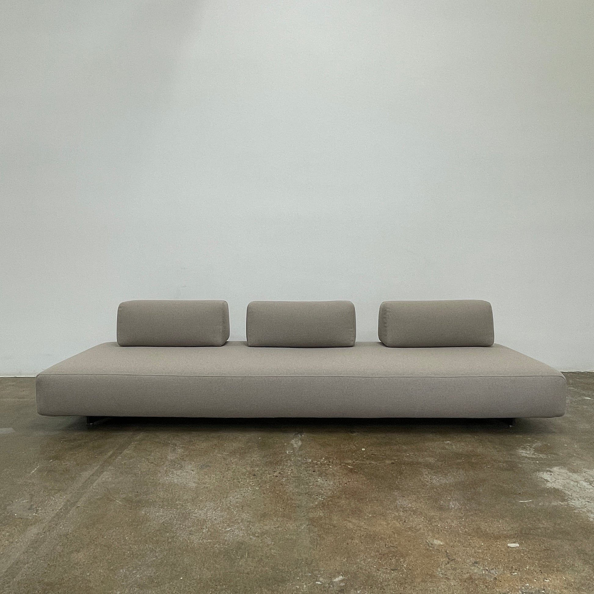 A minimalist gray Paola Lenti Orlando sofa bench from Modern Resale, featuring a 37" square design with one backrest and two rectangular cushions, is set against a plain white background.