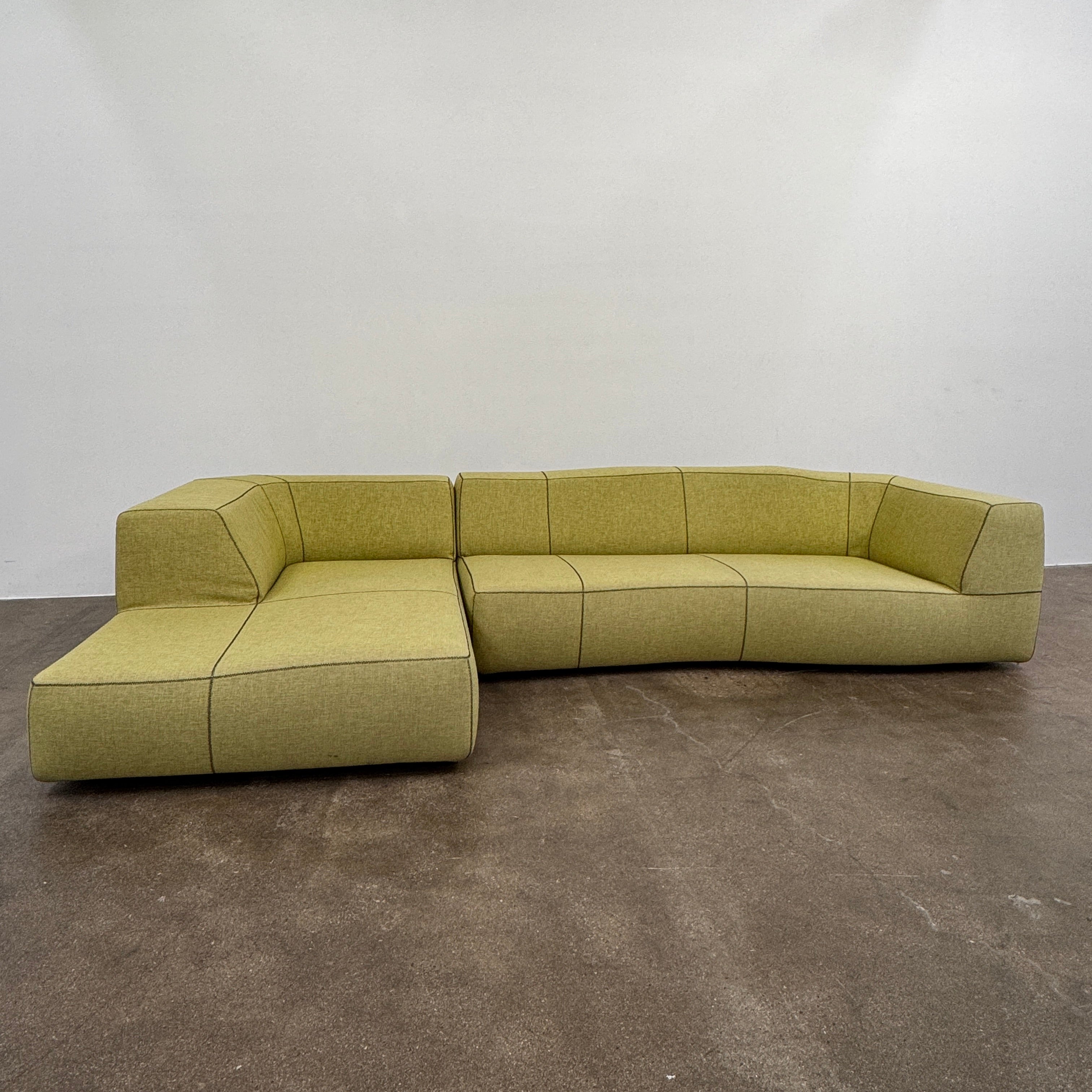 The B&B Italia Bend Sectional Sofa by B&B Italia features olive green fabric, black accent stitching, low backrests, and a geometric design inspired by Patricia Urquiola, shown on a plain white background.