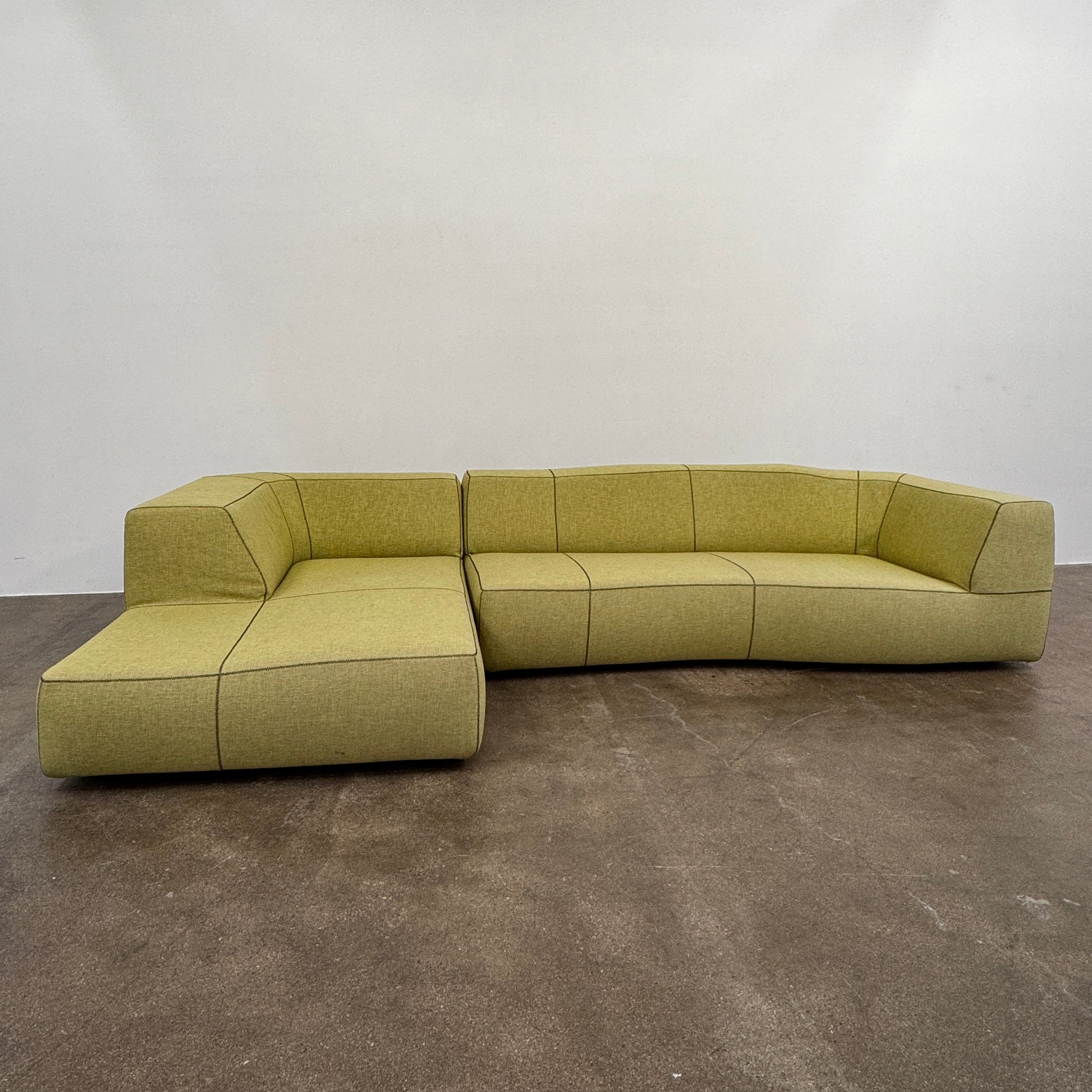 The B&B Italia Bend Sectional Sofa by B&B Italia features olive green fabric, black accent stitching, low backrests, and a geometric design inspired by Patricia Urquiola, shown on a plain white background.