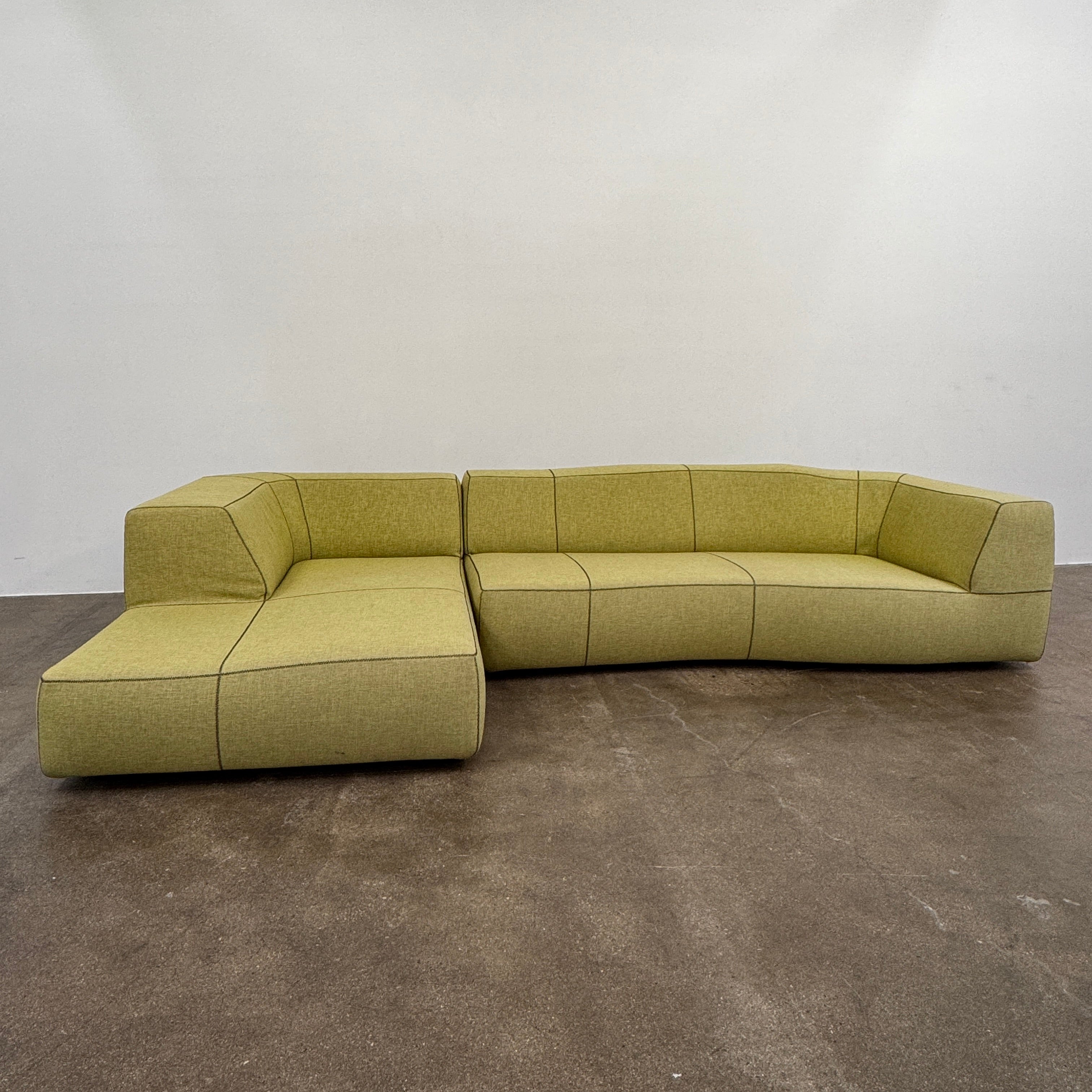 The B&B Italia Bend Sectional Sofa by B&B Italia features olive green fabric, black accent stitching, low backrests, and a geometric design inspired by Patricia Urquiola, shown on a plain white background.