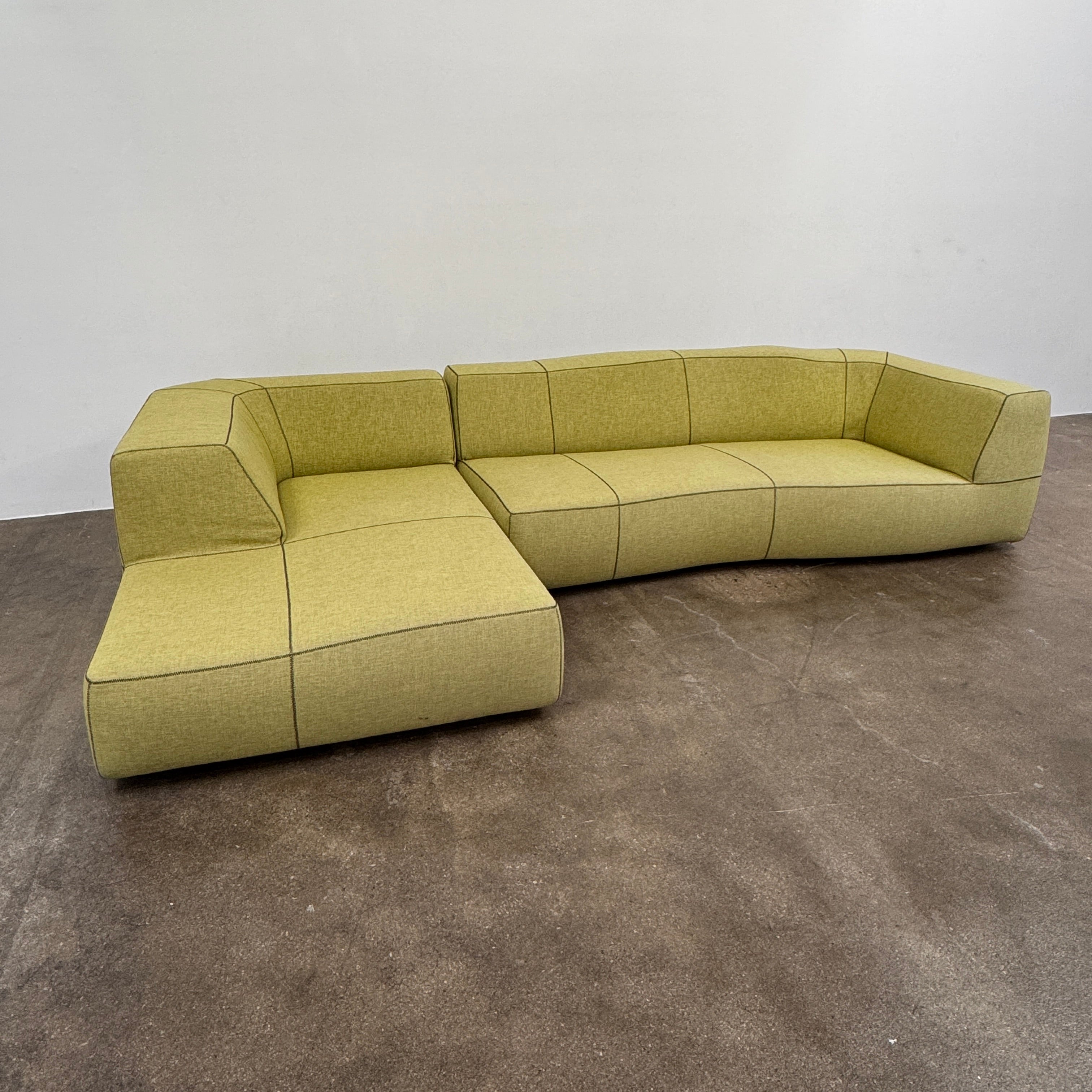 The B&B Italia Bend Sectional Sofa by B&B Italia features olive green fabric, black accent stitching, low backrests, and a geometric design inspired by Patricia Urquiola, shown on a plain white background.