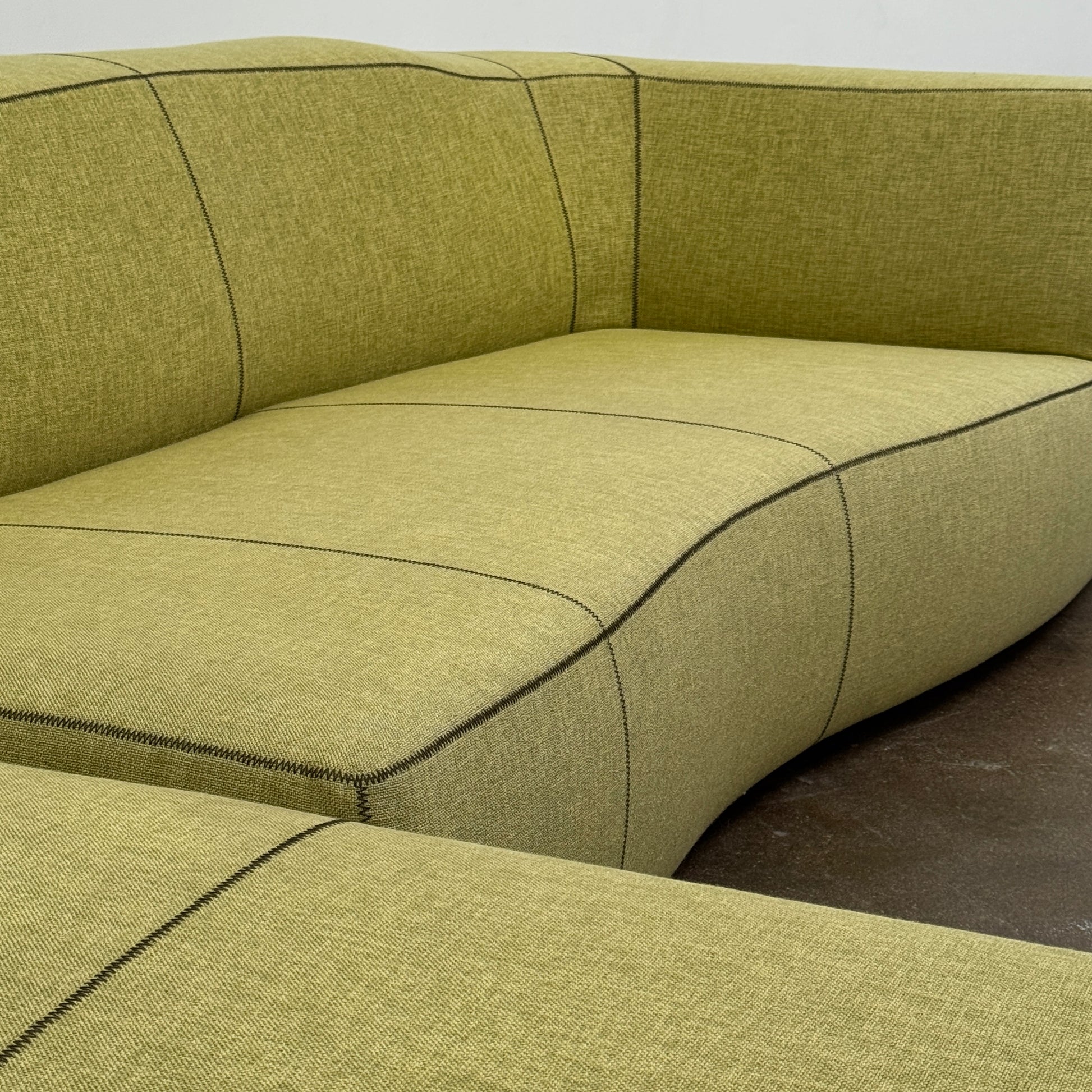 The B&B Italia Bend Sectional Sofa by B&B Italia features olive green fabric, black accent stitching, low backrests, and a geometric design inspired by Patricia Urquiola, shown on a plain white background.