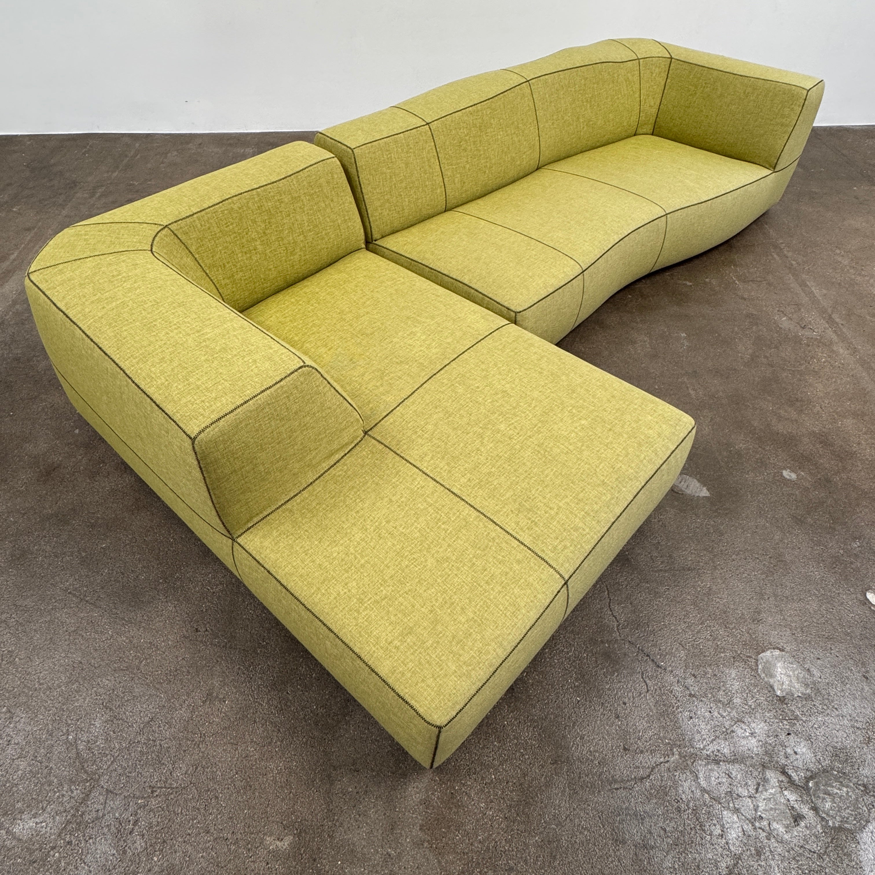 The B&B Italia Bend Sectional Sofa by B&B Italia features olive green fabric, black accent stitching, low backrests, and a geometric design inspired by Patricia Urquiola, shown on a plain white background.