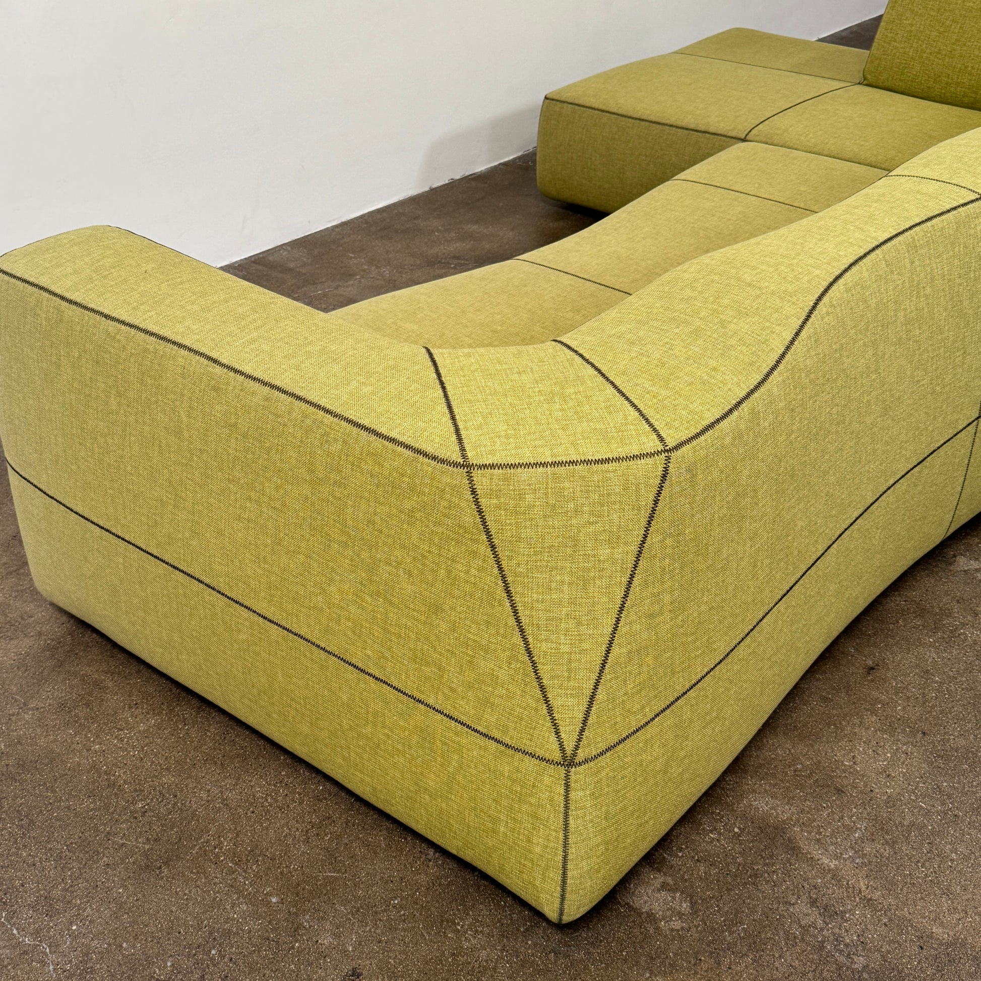 The B&B Italia Bend Sectional Sofa by B&B Italia features olive green fabric, black accent stitching, low backrests, and a geometric design inspired by Patricia Urquiola, shown on a plain white background.