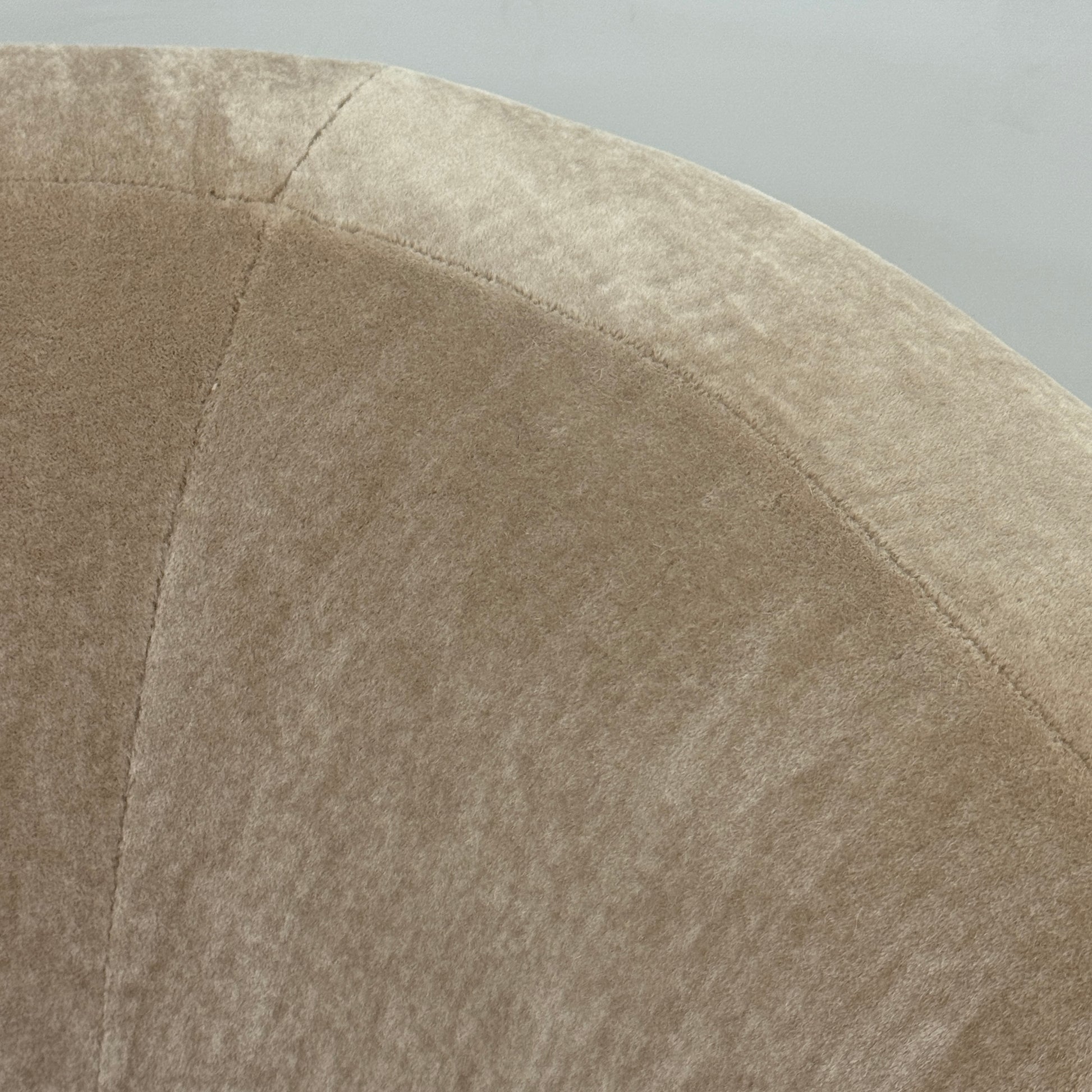 The tan, modern Holly Hunt Caste Malta Sofa with rounded edges sits stylishly on a polished concrete floor against a white wall, showcasing minimalist design inspired by Holly Hunt’s signature aesthetic.