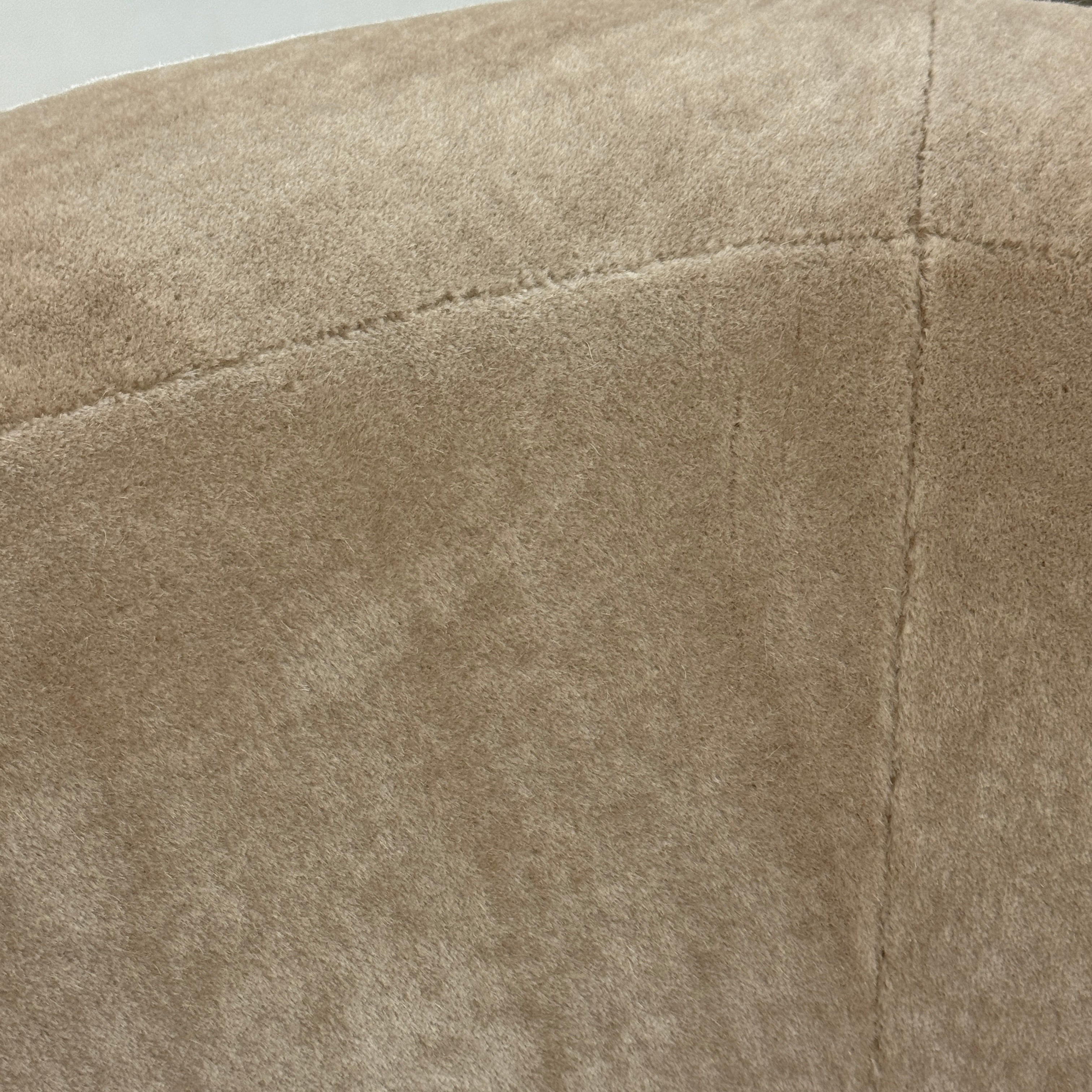 The tan, modern Holly Hunt Caste Malta Sofa with rounded edges sits stylishly on a polished concrete floor against a white wall, showcasing minimalist design inspired by Holly Hunt’s signature aesthetic.