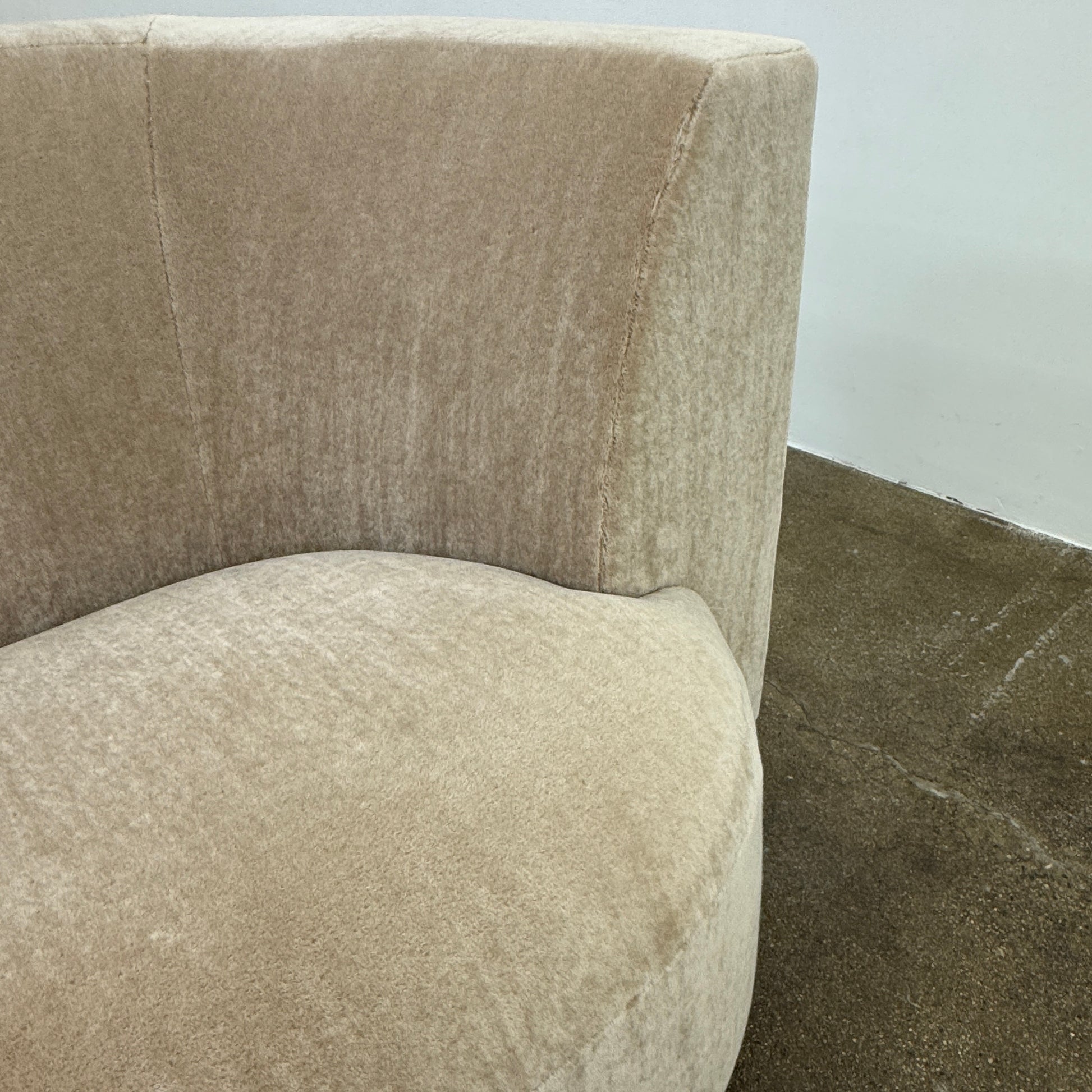 The tan, modern Holly Hunt Caste Malta Sofa with rounded edges sits stylishly on a polished concrete floor against a white wall, showcasing minimalist design inspired by Holly Hunt’s signature aesthetic.