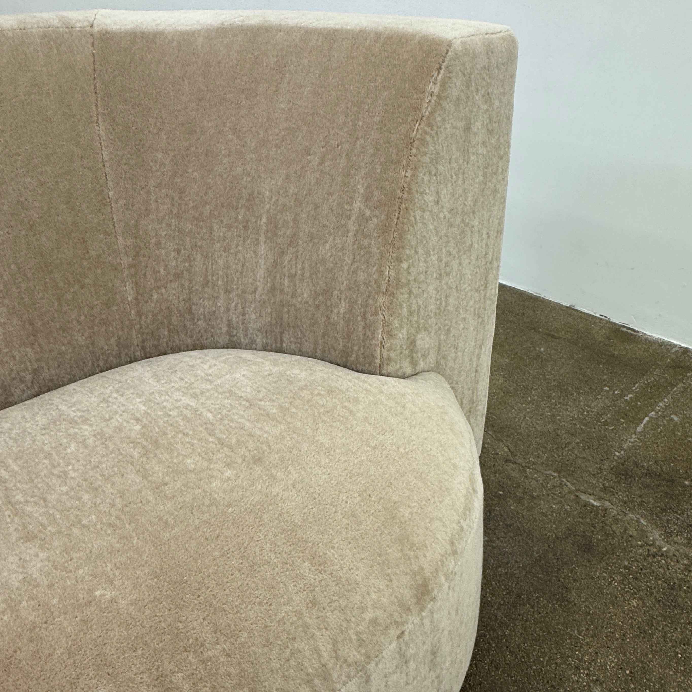 The tan, modern Holly Hunt Caste Malta Sofa with rounded edges sits stylishly on a polished concrete floor against a white wall, showcasing minimalist design inspired by Holly Hunt’s signature aesthetic.