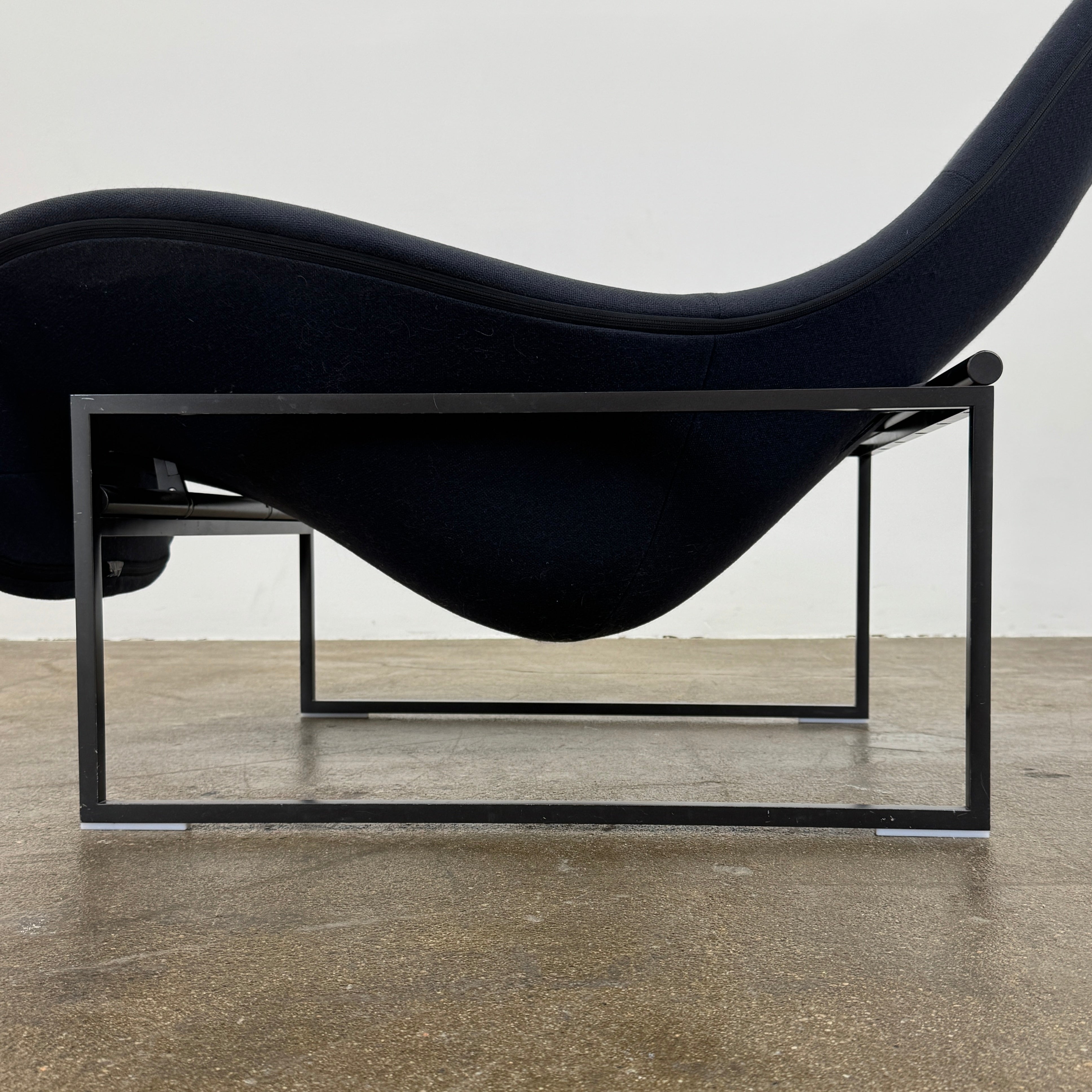 A B&B Italia Mart Relax Armchair with tilting mechanism and fabric seat by B&B Italia, featuring curved cushioned seating and a minimalist metal frame, sits on a concrete floor against a plain light-colored wall.