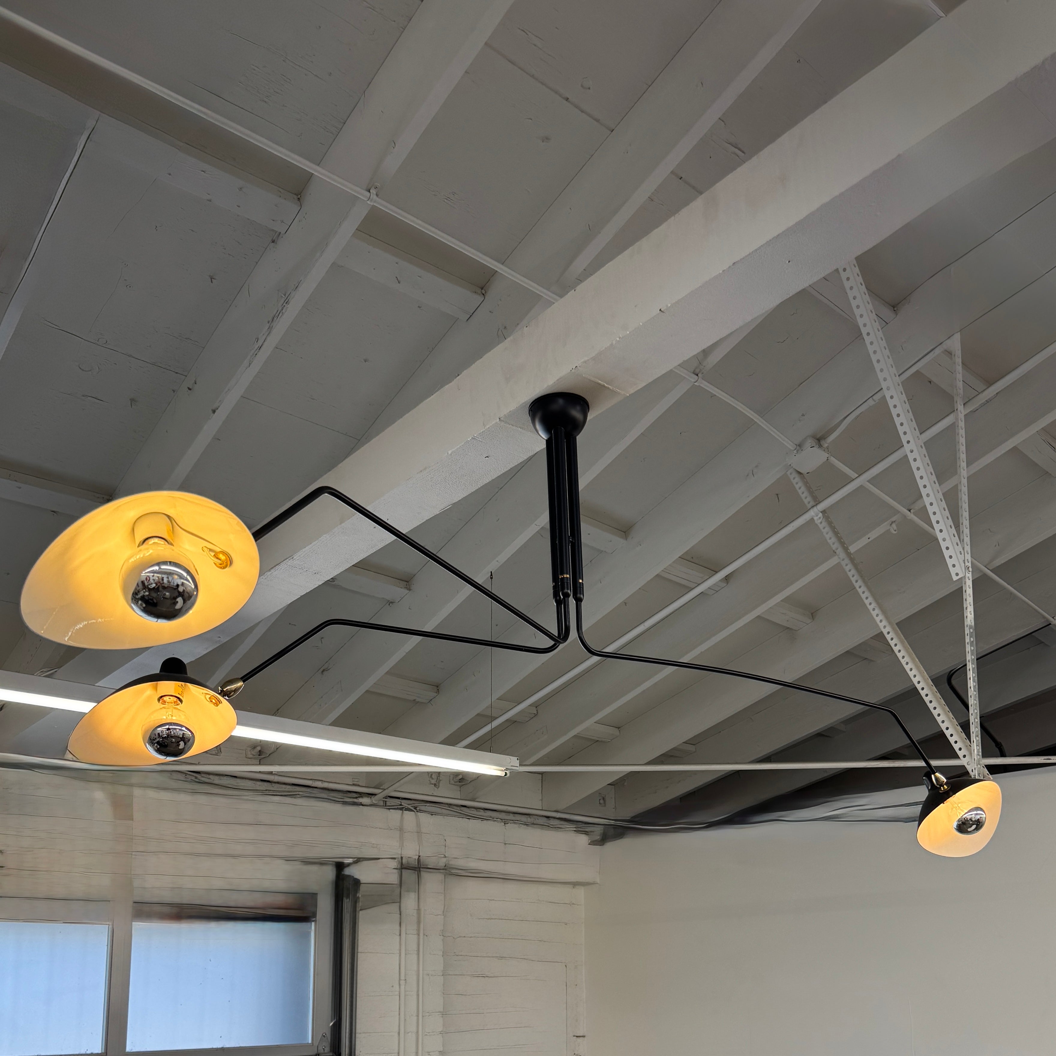 The Serge Mouille 3 Arm Ceiling Light by Serge Mouille features three black conical shades on adjustable metal arms from a central ceiling mount, displayed against a plain white background.