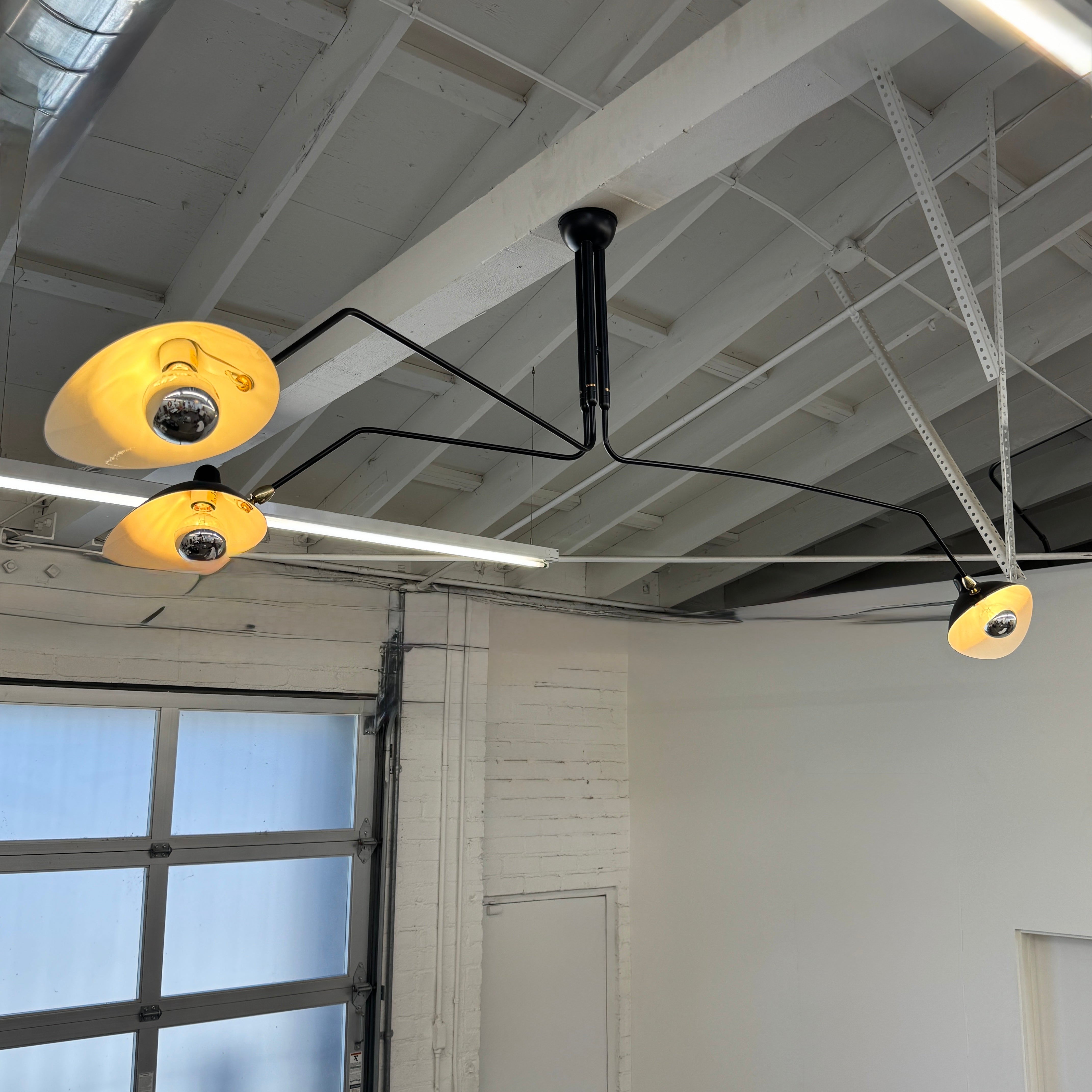 The Serge Mouille 3 Arm Ceiling Light by Serge Mouille features three black conical shades on adjustable metal arms from a central ceiling mount, displayed against a plain white background.