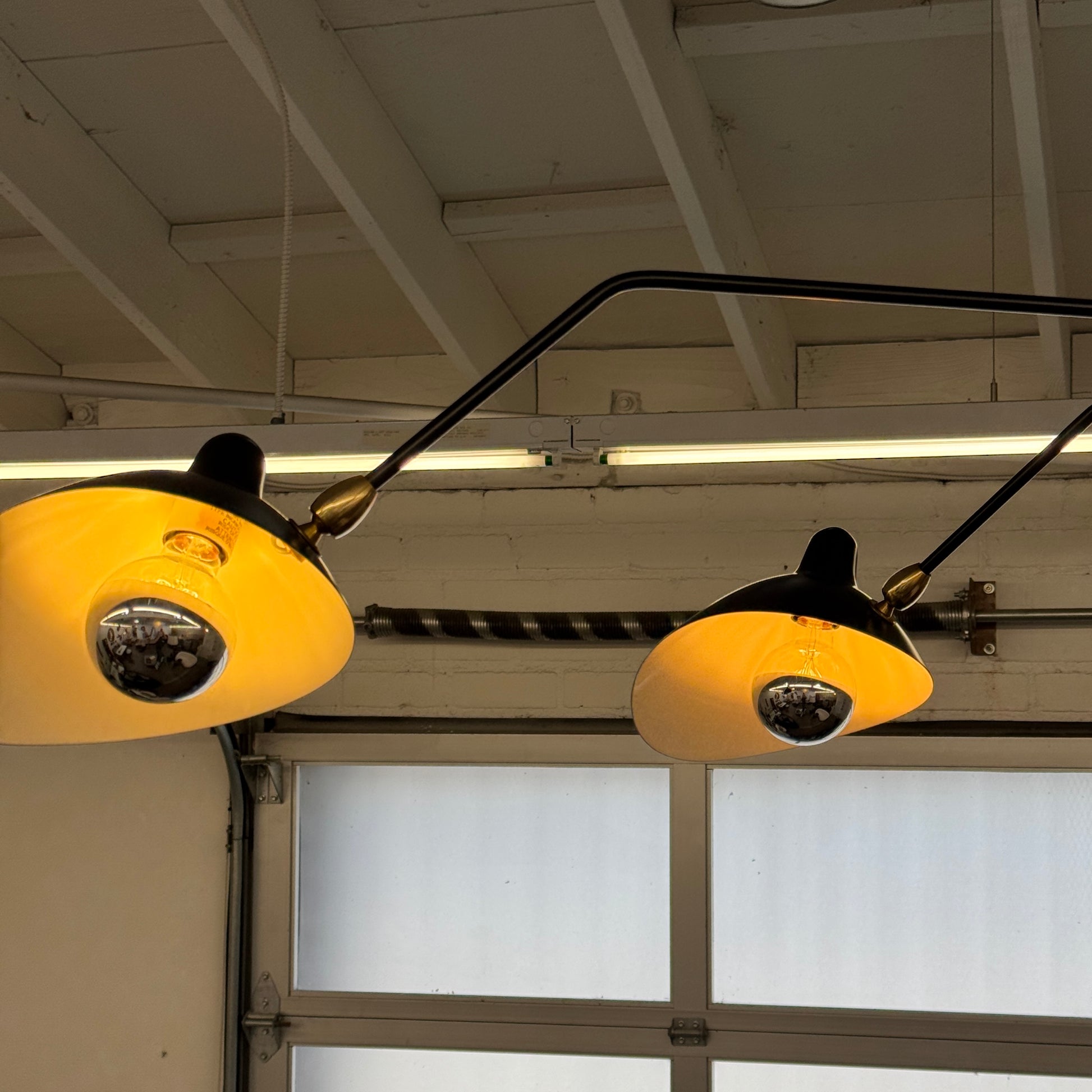 The Serge Mouille 3 Arm Ceiling Light by Serge Mouille features three black conical shades on adjustable metal arms from a central ceiling mount, displayed against a plain white background.