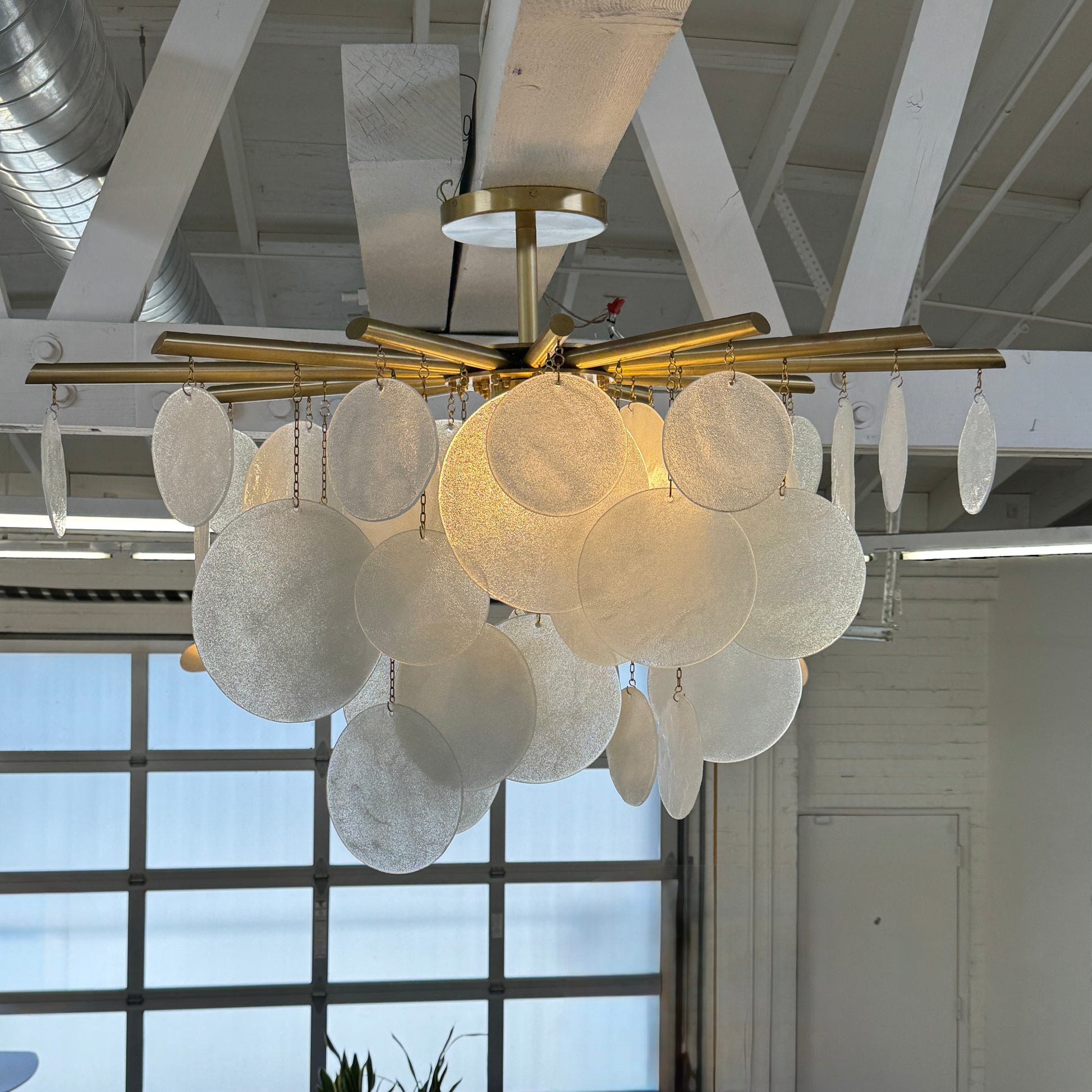 The Nimbu Medium Chandelier by Nimbu features a brass finish and layered frosted glass discs, creating a soft, warm glow—ideal as a contemporary centerpiece.