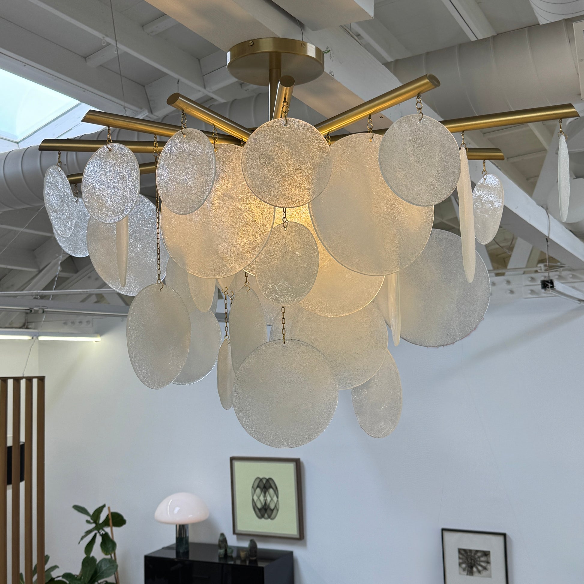 The Nimbu Medium Chandelier by Nimbu features a brass finish and layered frosted glass discs, creating a soft, warm glow—ideal as a contemporary centerpiece.