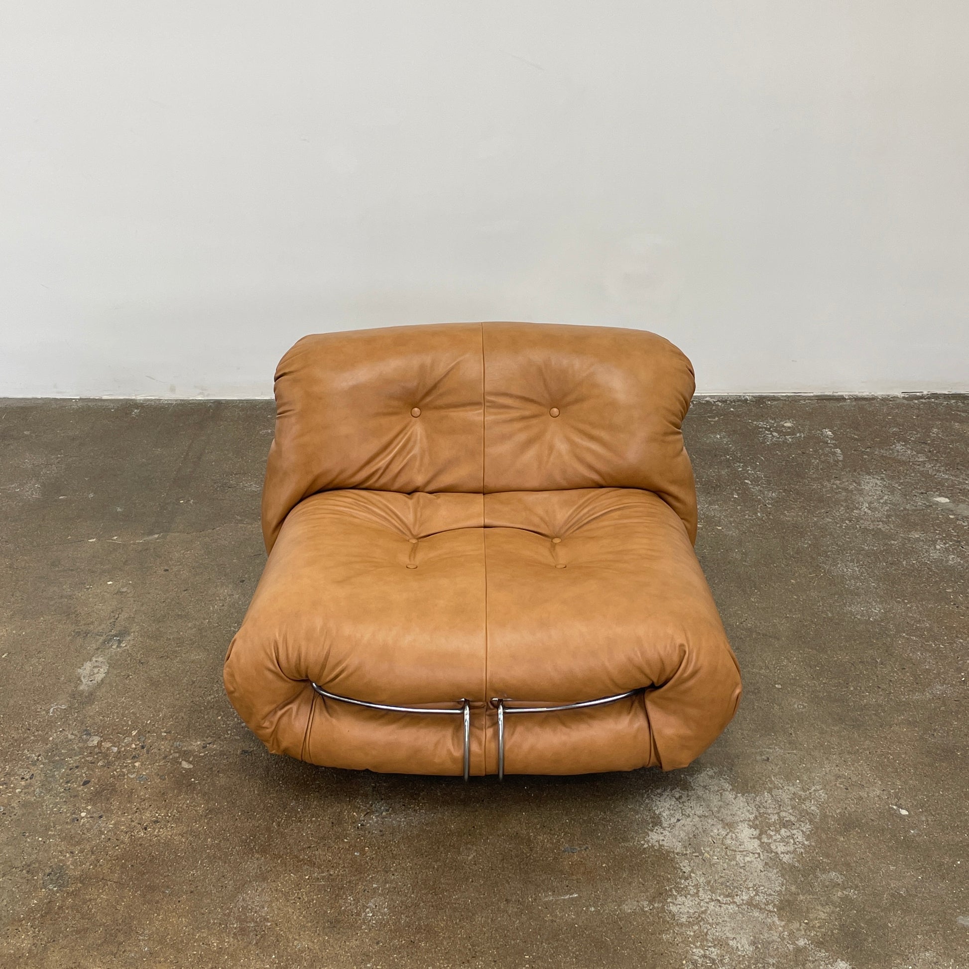 A set of two tan leather lounge chairs, echoing the vintage 1970s Cassina Soriana designs by Afra & Tobia Scarpa, showcases tufted backrests and tubular metal frames on a plain white background.