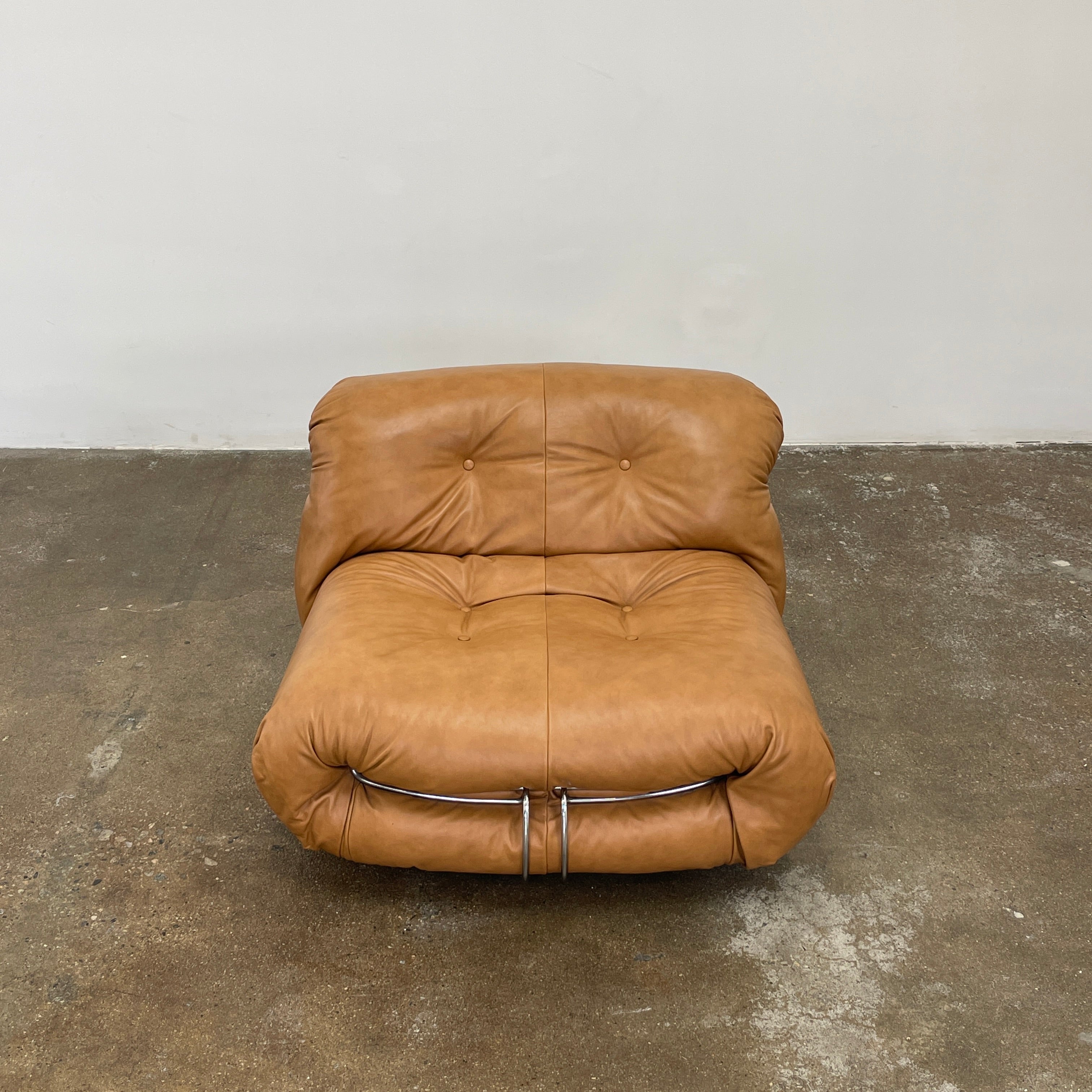 A set of two tan leather lounge chairs, echoing the vintage 1970s Cassina Soriana designs by Afra & Tobia Scarpa, showcases tufted backrests and tubular metal frames on a plain white background.
