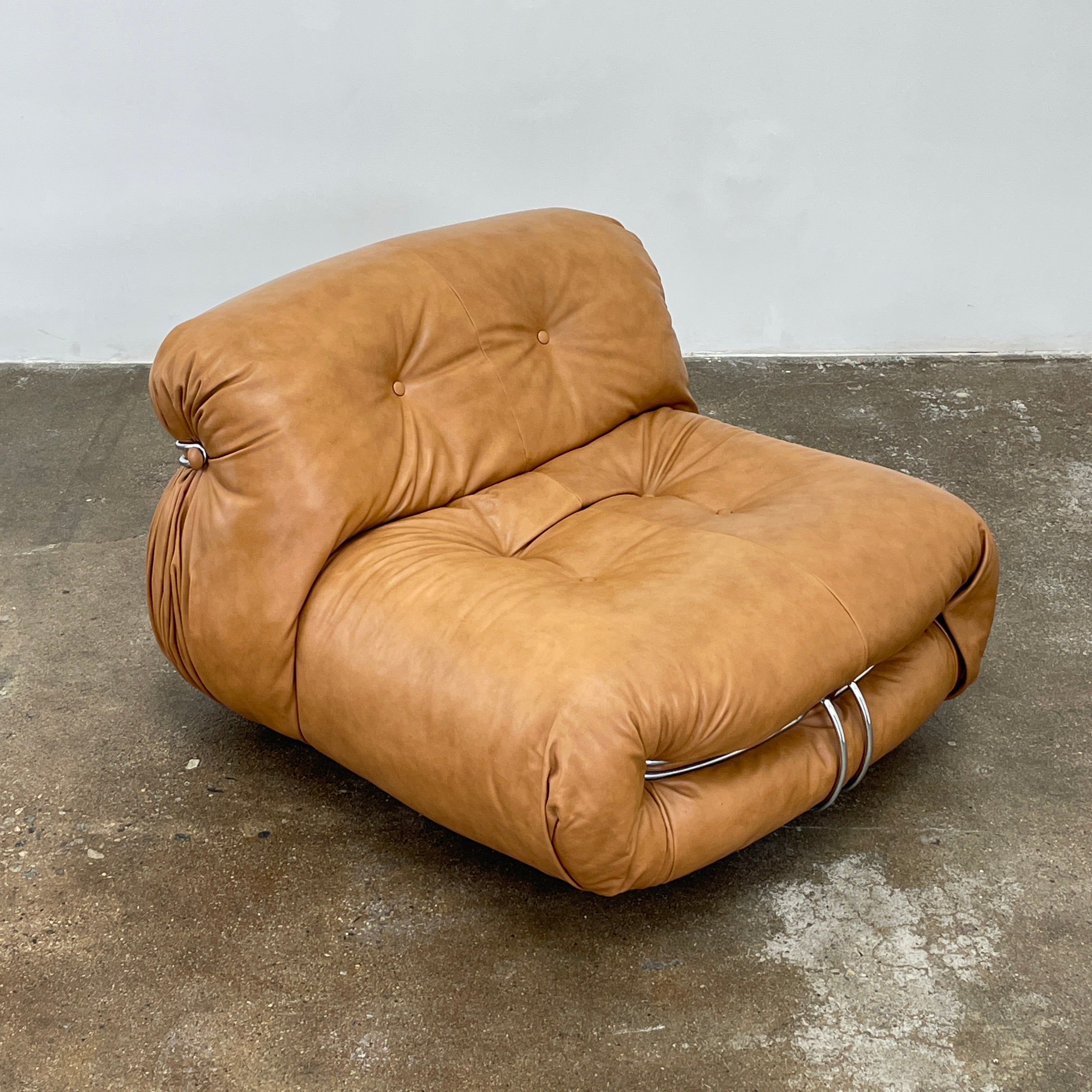 A set of two tan leather lounge chairs, echoing the vintage 1970s Cassina Soriana designs by Afra & Tobia Scarpa, showcases tufted backrests and tubular metal frames on a plain white background.