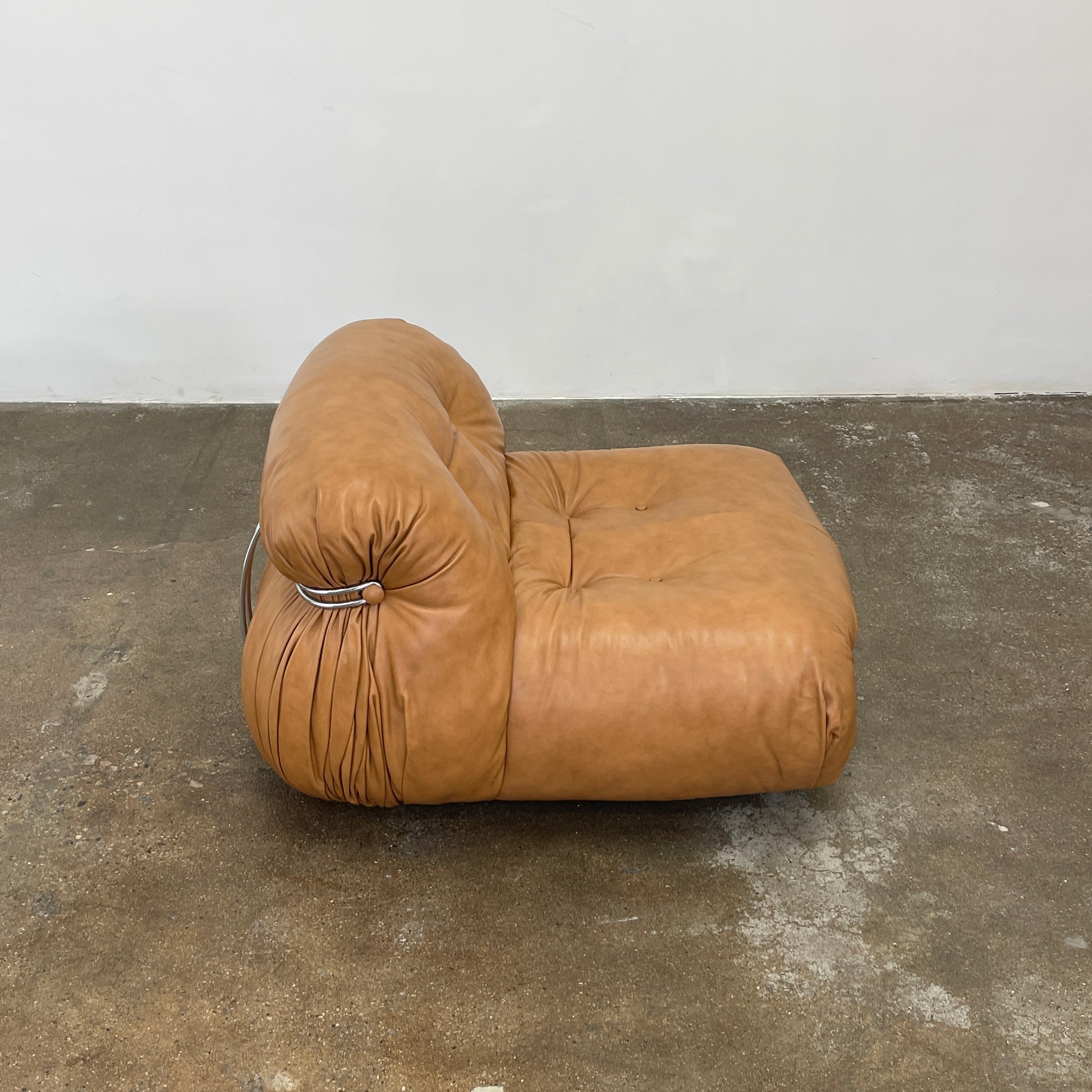 A set of two tan leather lounge chairs, echoing the vintage 1970s Cassina Soriana designs by Afra & Tobia Scarpa, showcases tufted backrests and tubular metal frames on a plain white background.