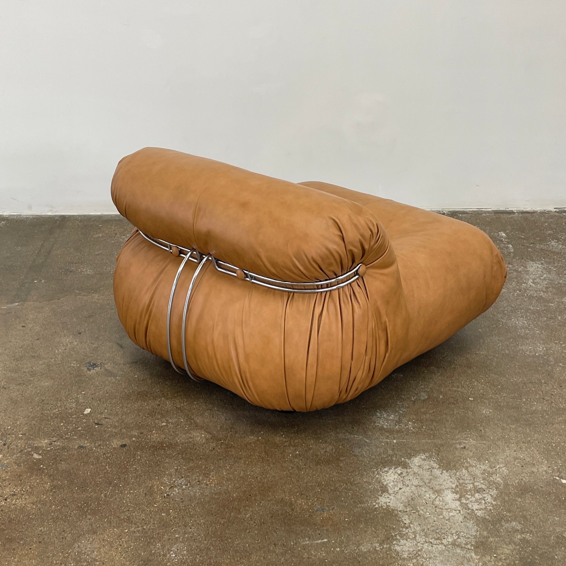 A set of two tan leather lounge chairs, echoing the vintage 1970s Cassina Soriana designs by Afra & Tobia Scarpa, showcases tufted backrests and tubular metal frames on a plain white background.