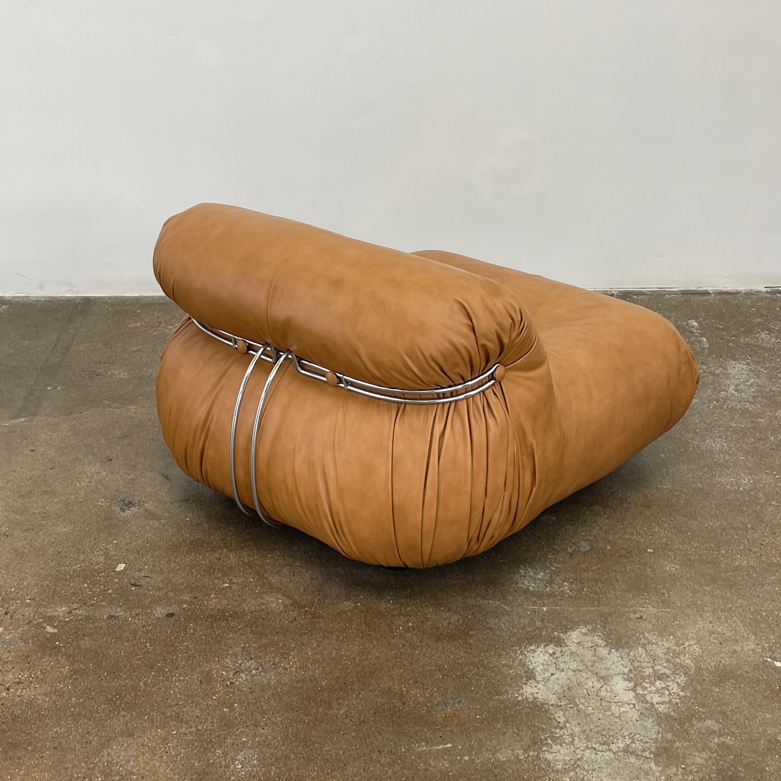 A set of two tan leather lounge chairs, echoing the vintage 1970s Cassina Soriana designs by Afra & Tobia Scarpa, showcases tufted backrests and tubular metal frames on a plain white background.