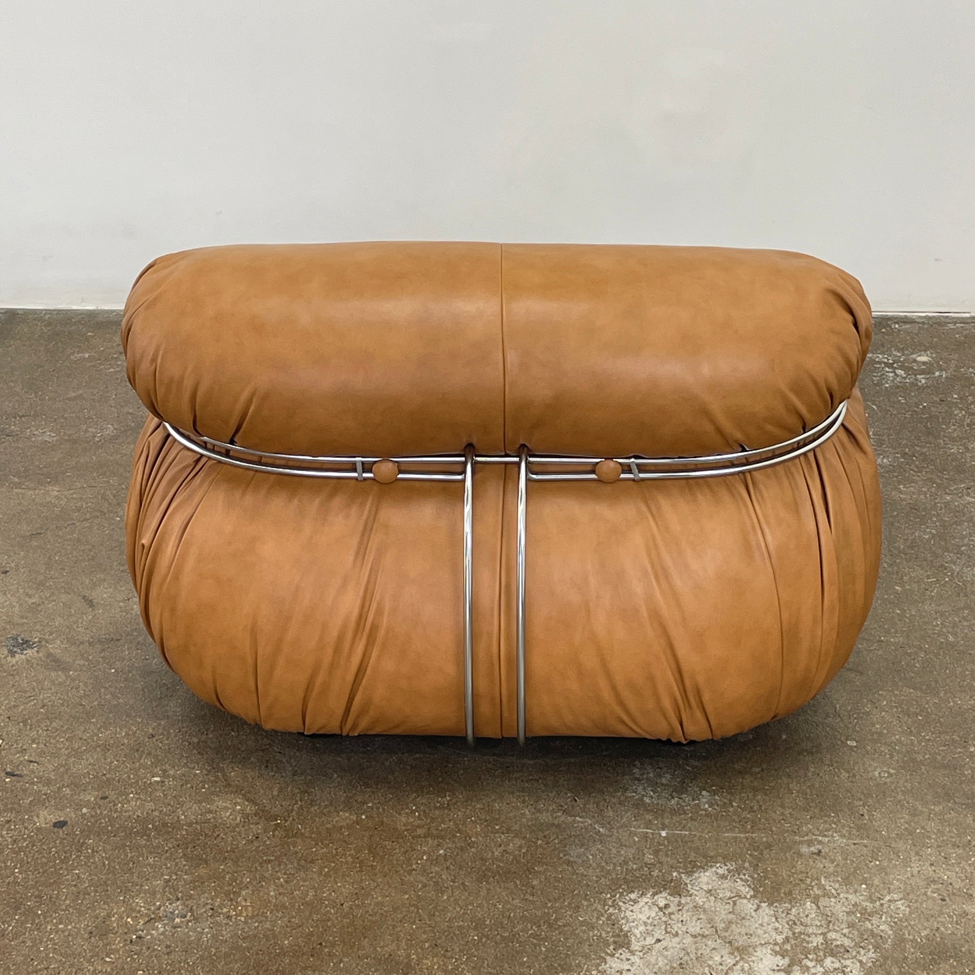 A set of two tan leather lounge chairs, echoing the vintage 1970s Cassina Soriana designs by Afra & Tobia Scarpa, showcases tufted backrests and tubular metal frames on a plain white background.