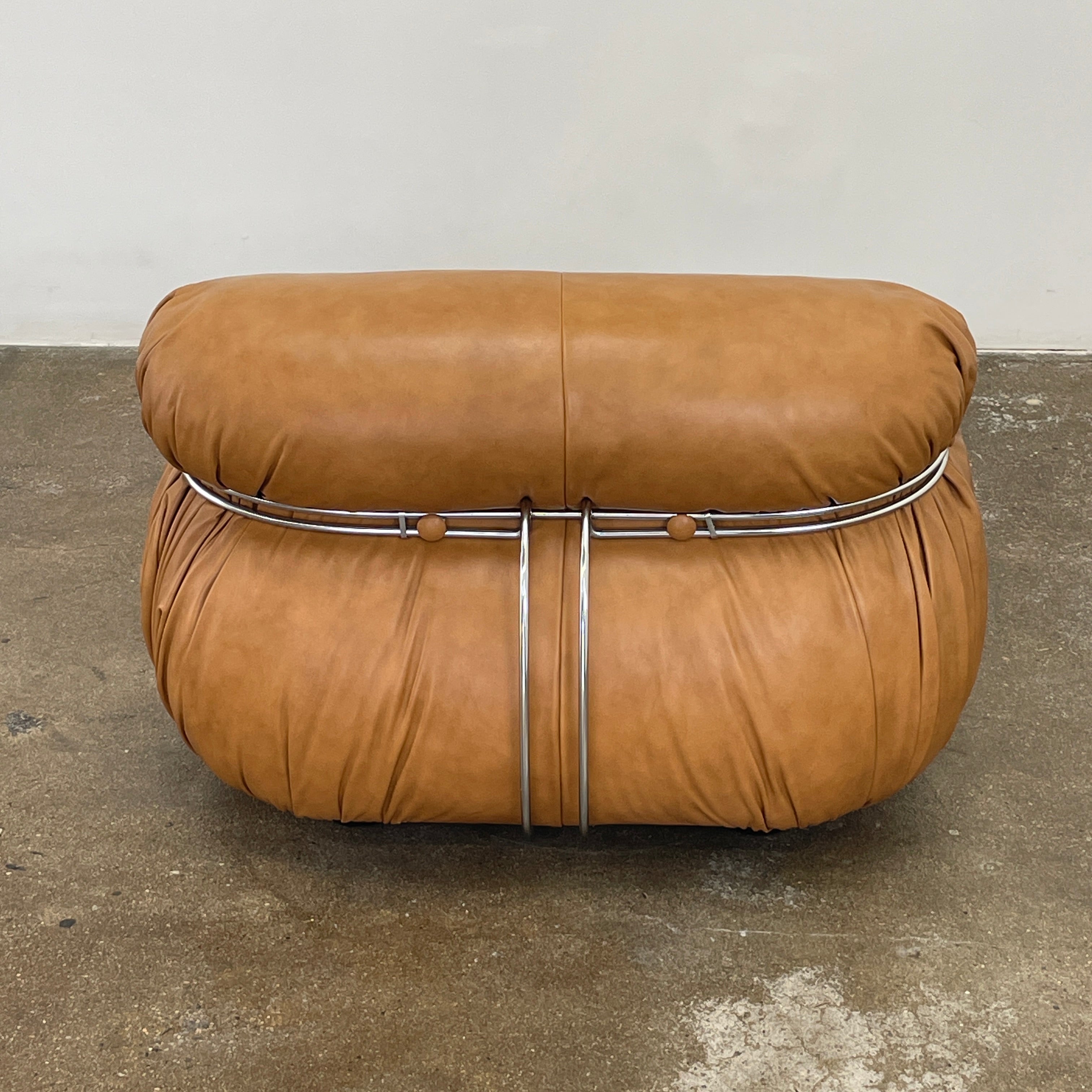 A set of two tan leather lounge chairs, echoing the vintage 1970s Cassina Soriana designs by Afra & Tobia Scarpa, showcases tufted backrests and tubular metal frames on a plain white background.