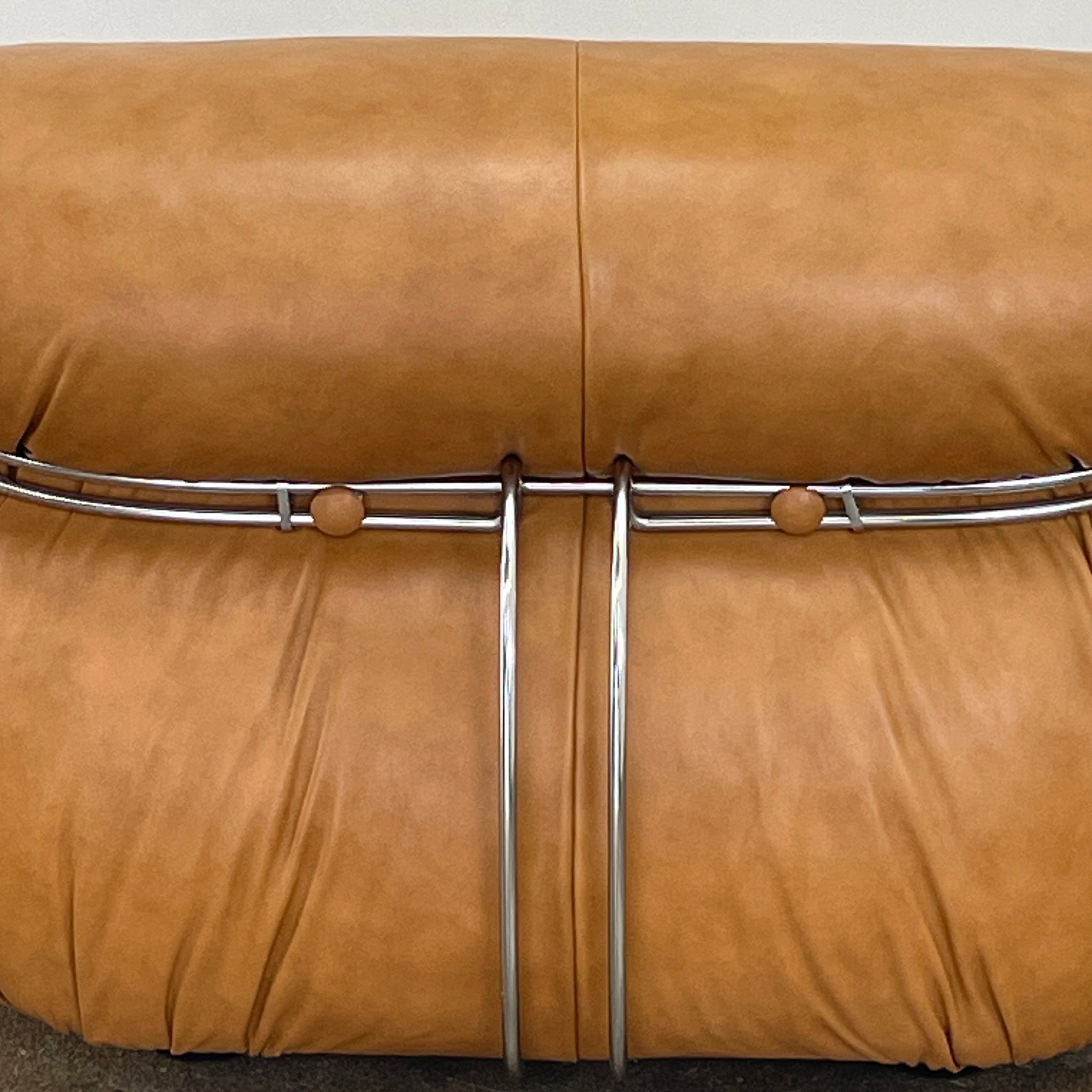A set of two tan leather lounge chairs, echoing the vintage 1970s Cassina Soriana designs by Afra & Tobia Scarpa, showcases tufted backrests and tubular metal frames on a plain white background.