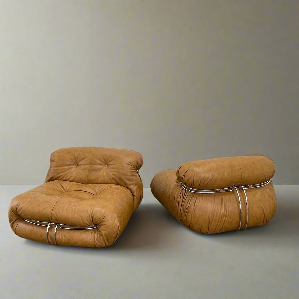 A set of two tan leather lounge chairs, echoing the vintage 1970s Cassina Soriana designs by Afra & Tobia Scarpa, showcases tufted backrests and tubular metal frames on a plain white background.
