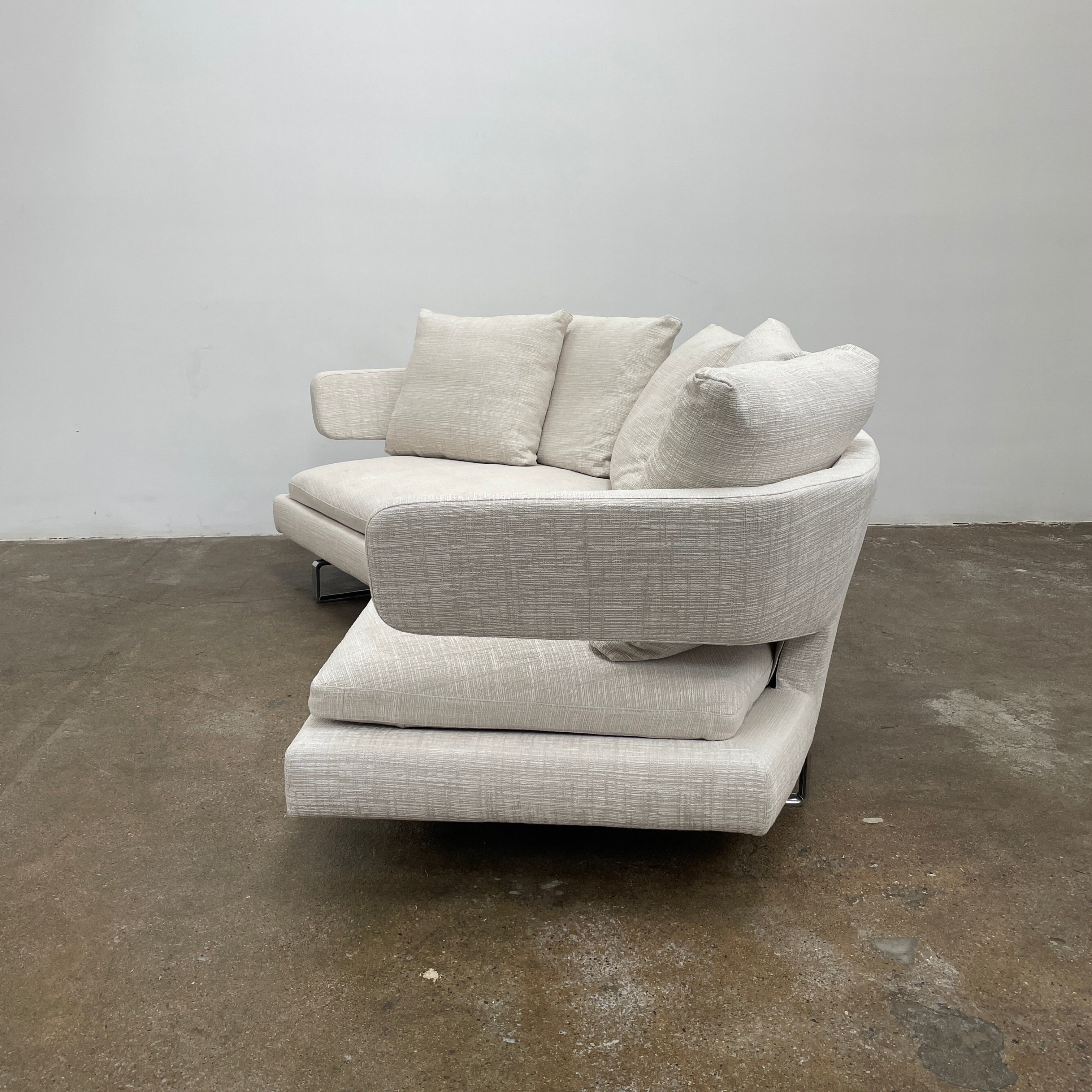 Experience the B&B Italia Arne Sofa, a modern off-white masterpiece with five plush cushions and cylindrical armrests. Designed by Antonio Citterio, it features sleek metal legs set against a crisp background.