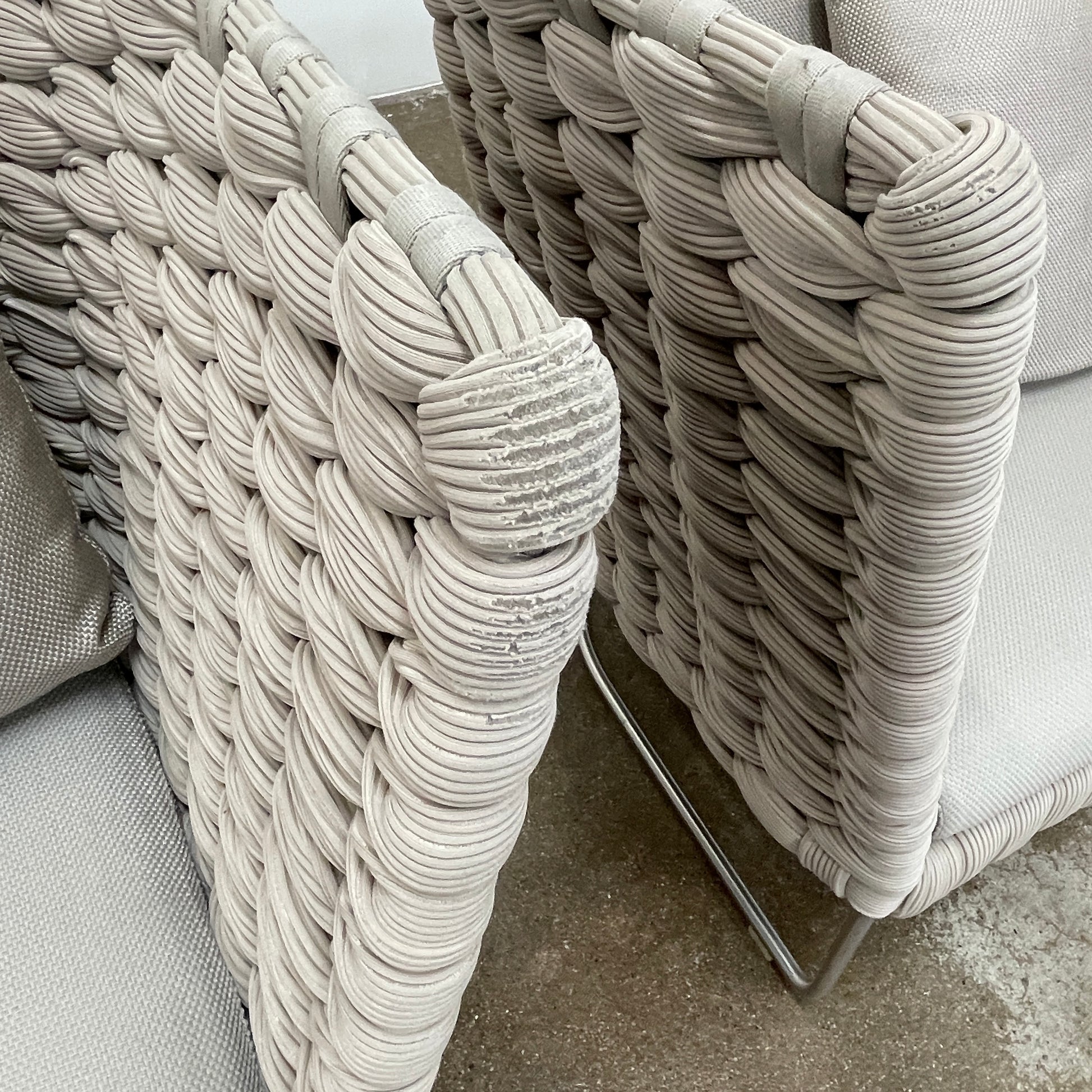 The Paola Lenti Ami Outdoor Armchair by Paola Lenti features a large weave frame, light gray cushions, and a metal base, all set against a plain white background.