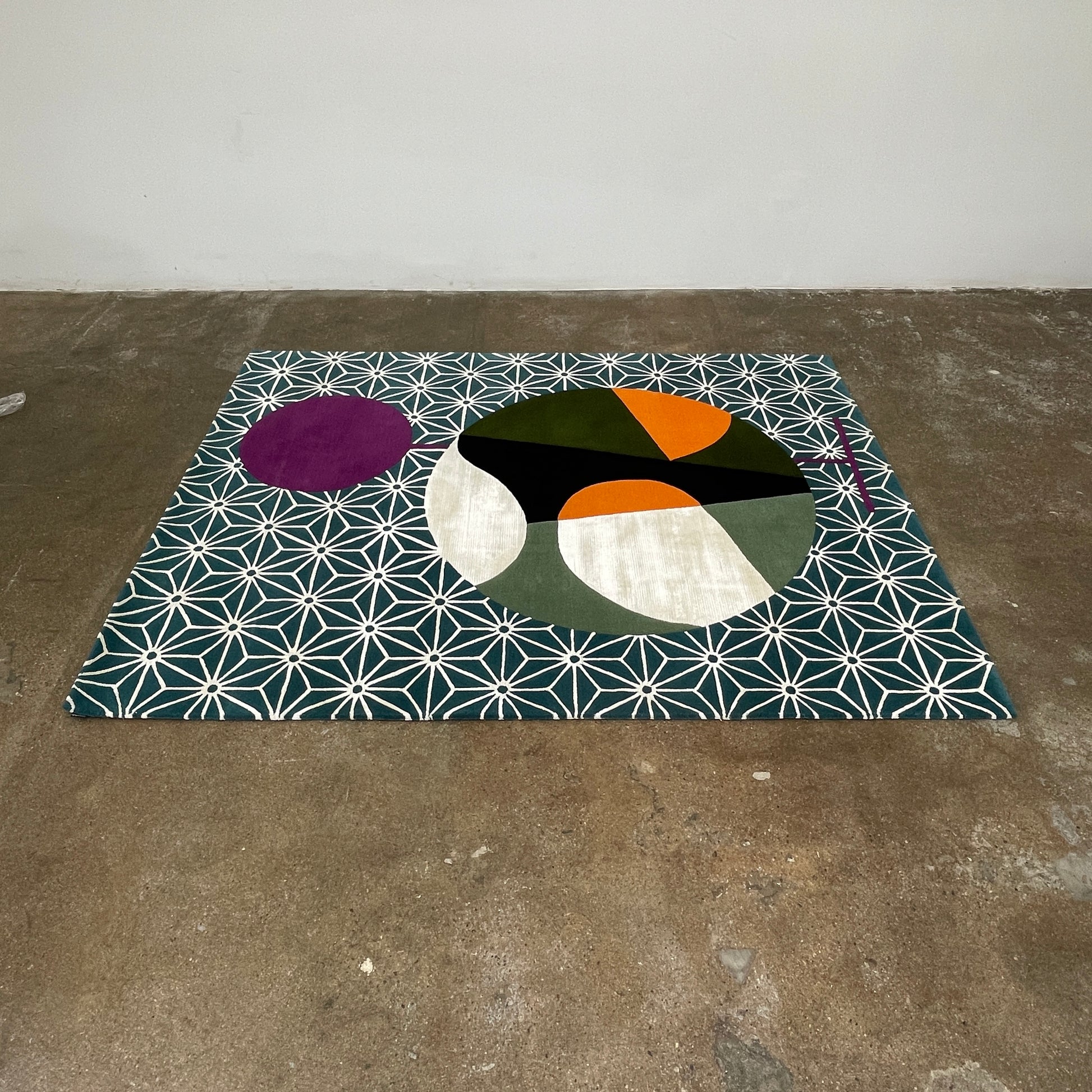 The Maison Dada Japanese Abstraction No5 Rug showcases a geometric pattern with a striking central circle in orange, green, and cream. A smaller purple circle enhances the design, complemented by a white star pattern on a green background reminiscent of Japanese abstraction.