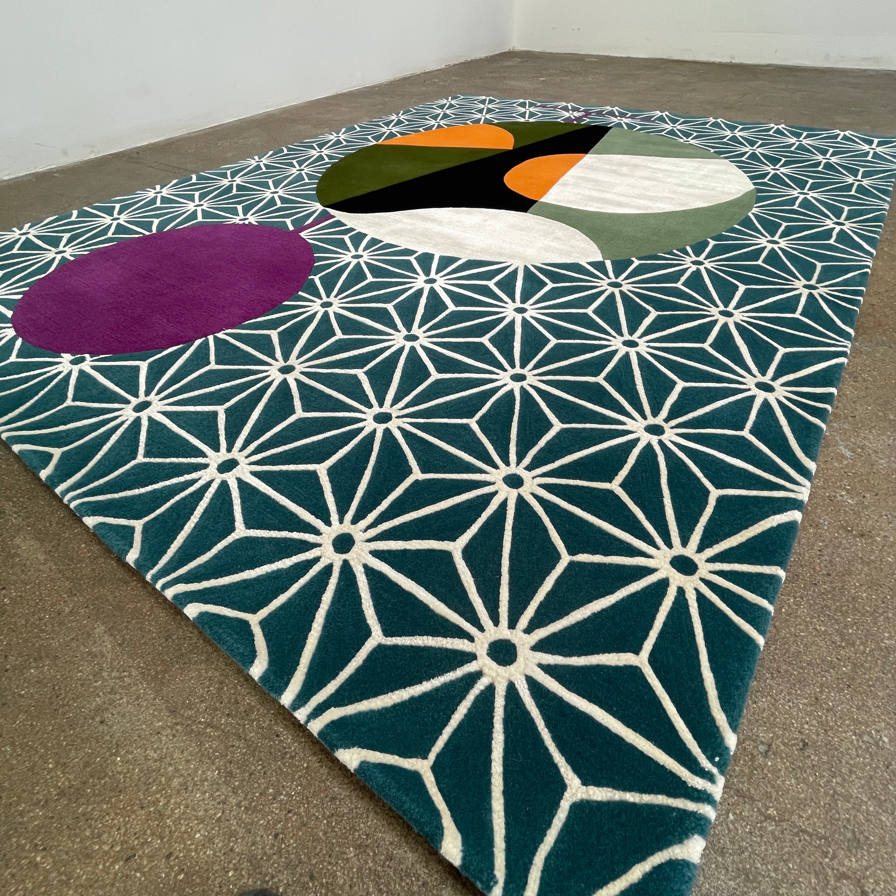 The Maison Dada Japanese Abstraction No5 Rug showcases a geometric pattern with a striking central circle in orange, green, and cream. A smaller purple circle enhances the design, complemented by a white star pattern on a green background reminiscent of Japanese abstraction.