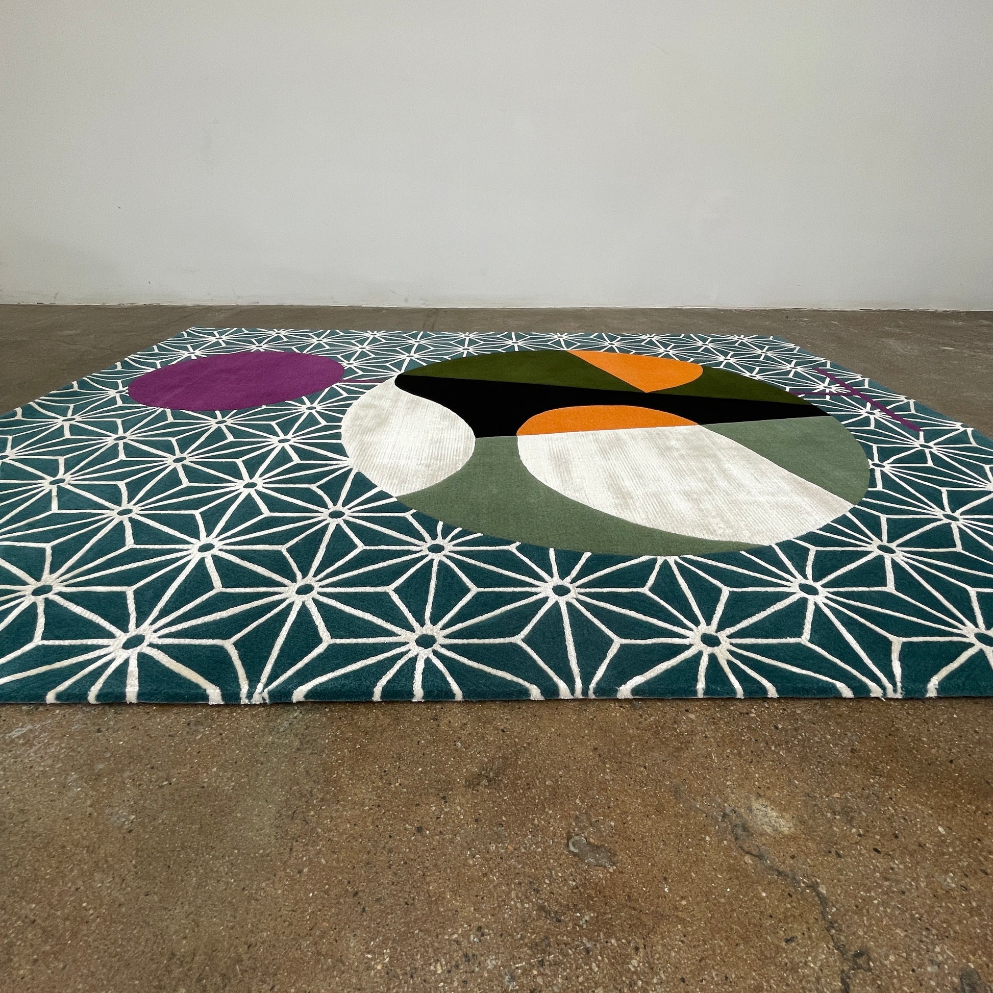 The Maison Dada Japanese Abstraction No5 Rug showcases a geometric pattern with a striking central circle in orange, green, and cream. A smaller purple circle enhances the design, complemented by a white star pattern on a green background reminiscent of Japanese abstraction.