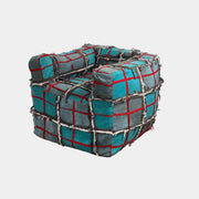 The Earth Landing Project Plaid Chair features boxy arms and patchwork teal, black, and red upholstery; frayed seams and irregular stitching create a rugged, textured look inspired by Earth Landing Project designs.