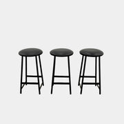A set of three Johanson Design Sputnik Counter Stools by Modern Resale, featuring round seats and metal legs, are arranged in a row on a concrete floor against a white wall, bringing enduring style to any space.