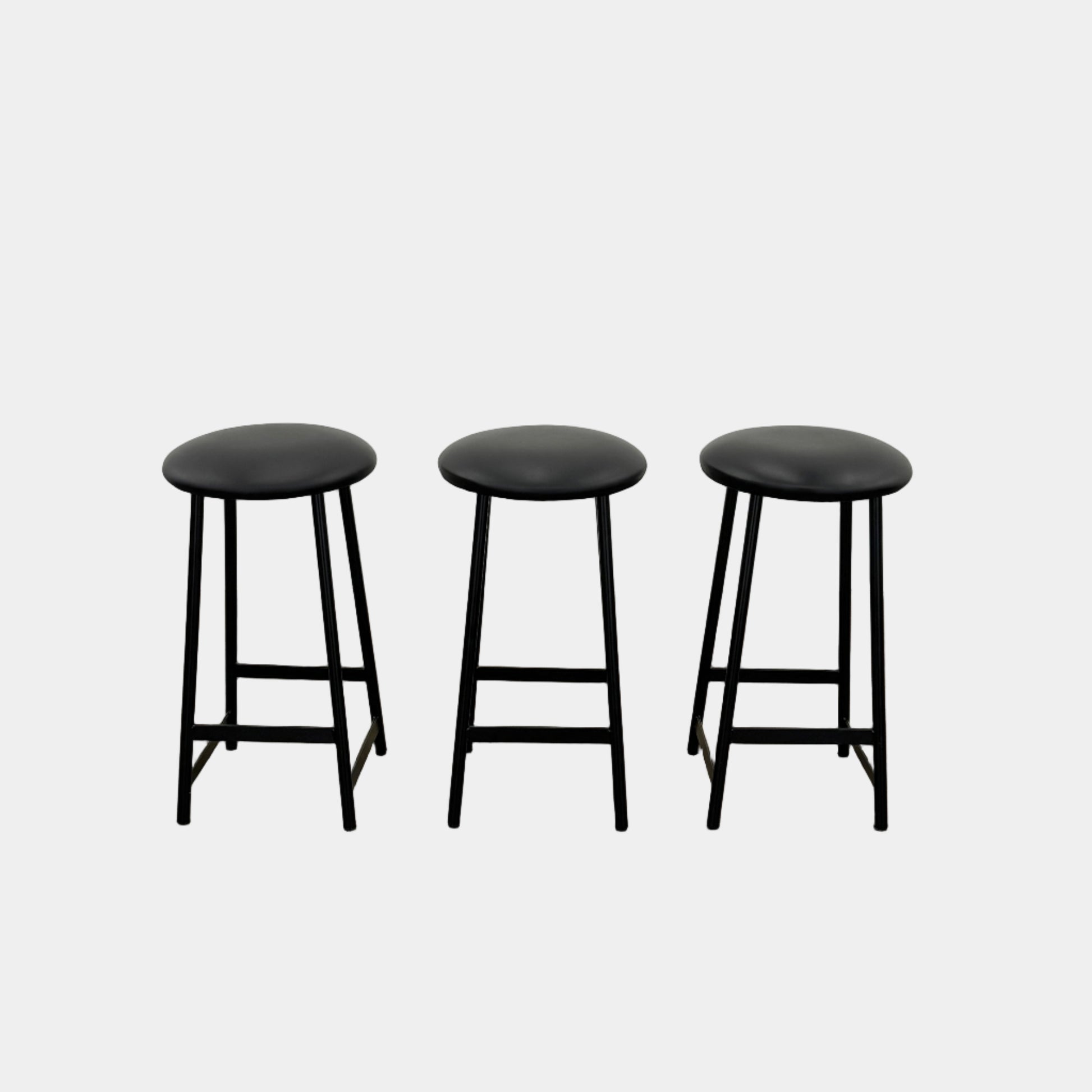 A set of three Johanson Design Sputnik Counter Stools by Modern Resale, featuring round seats and metal legs, are arranged in a row on a concrete floor against a white wall, bringing enduring style to any space.
