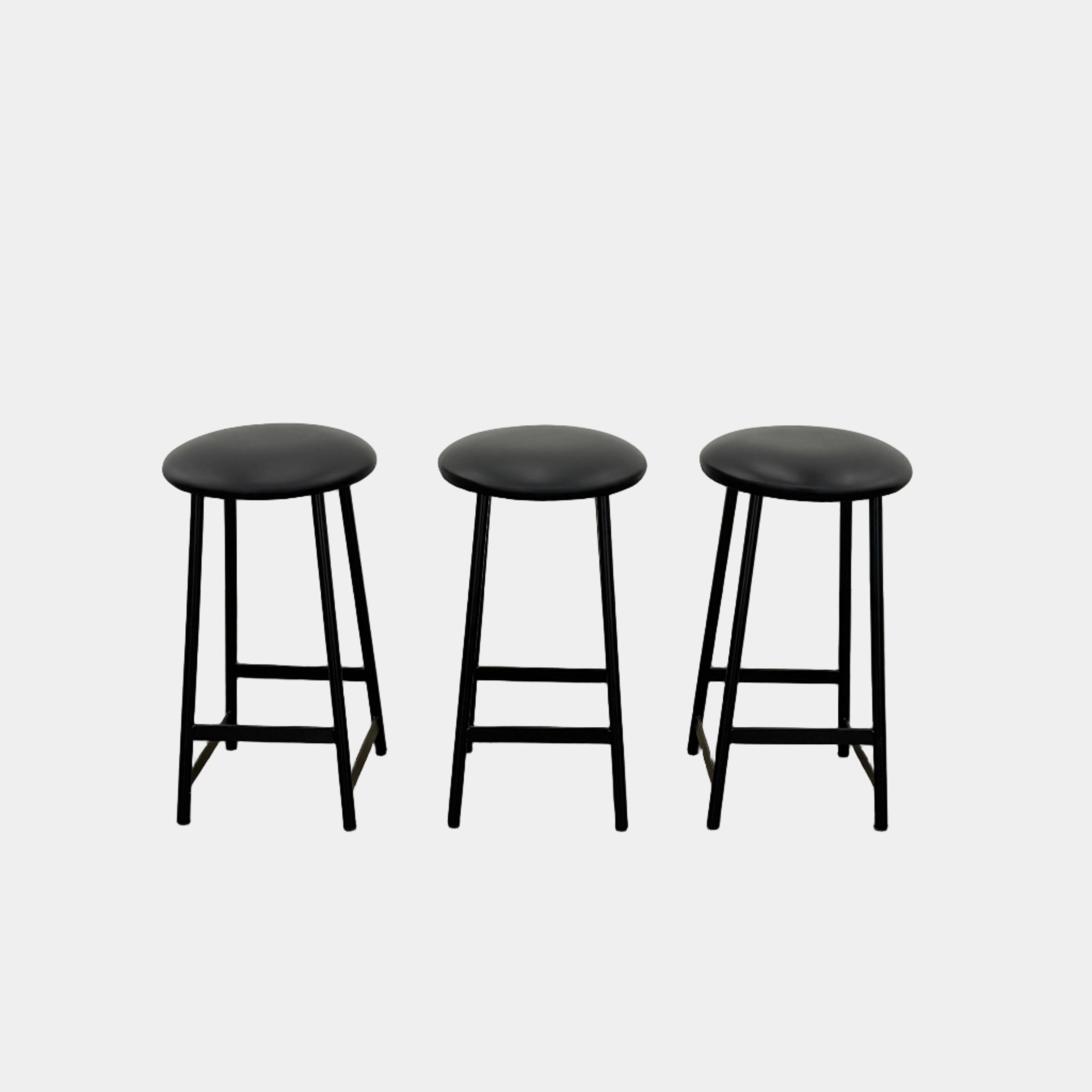 A set of three Johanson Design Sputnik Counter Stools by Modern Resale, featuring round seats and metal legs, are arranged in a row on a concrete floor against a white wall, bringing enduring style to any space.
