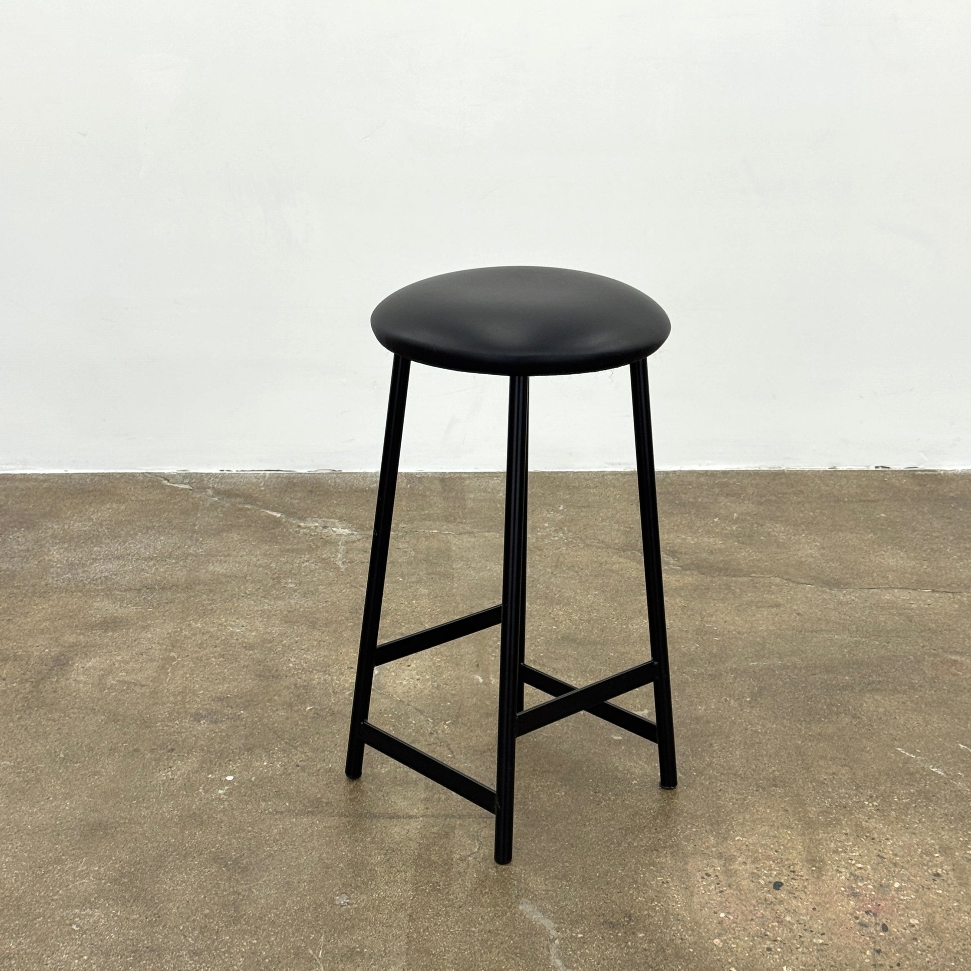 A set of three Johanson Design Sputnik Counter Stools by Modern Resale, featuring round seats and metal legs, are arranged in a row on a concrete floor against a white wall, bringing enduring style to any space.