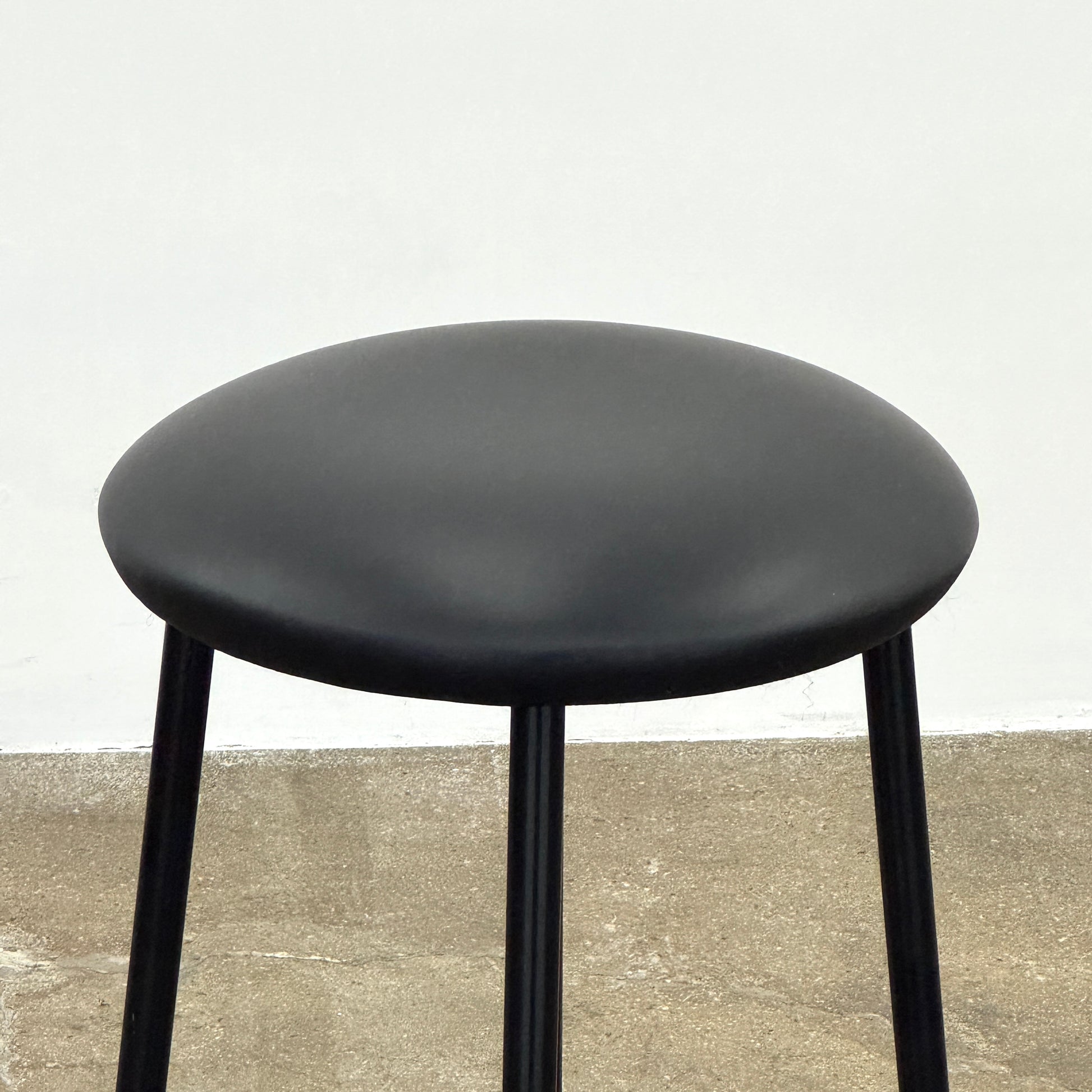 A set of three Johanson Design Sputnik Counter Stools by Modern Resale, featuring round seats and metal legs, are arranged in a row on a concrete floor against a white wall, bringing enduring style to any space.