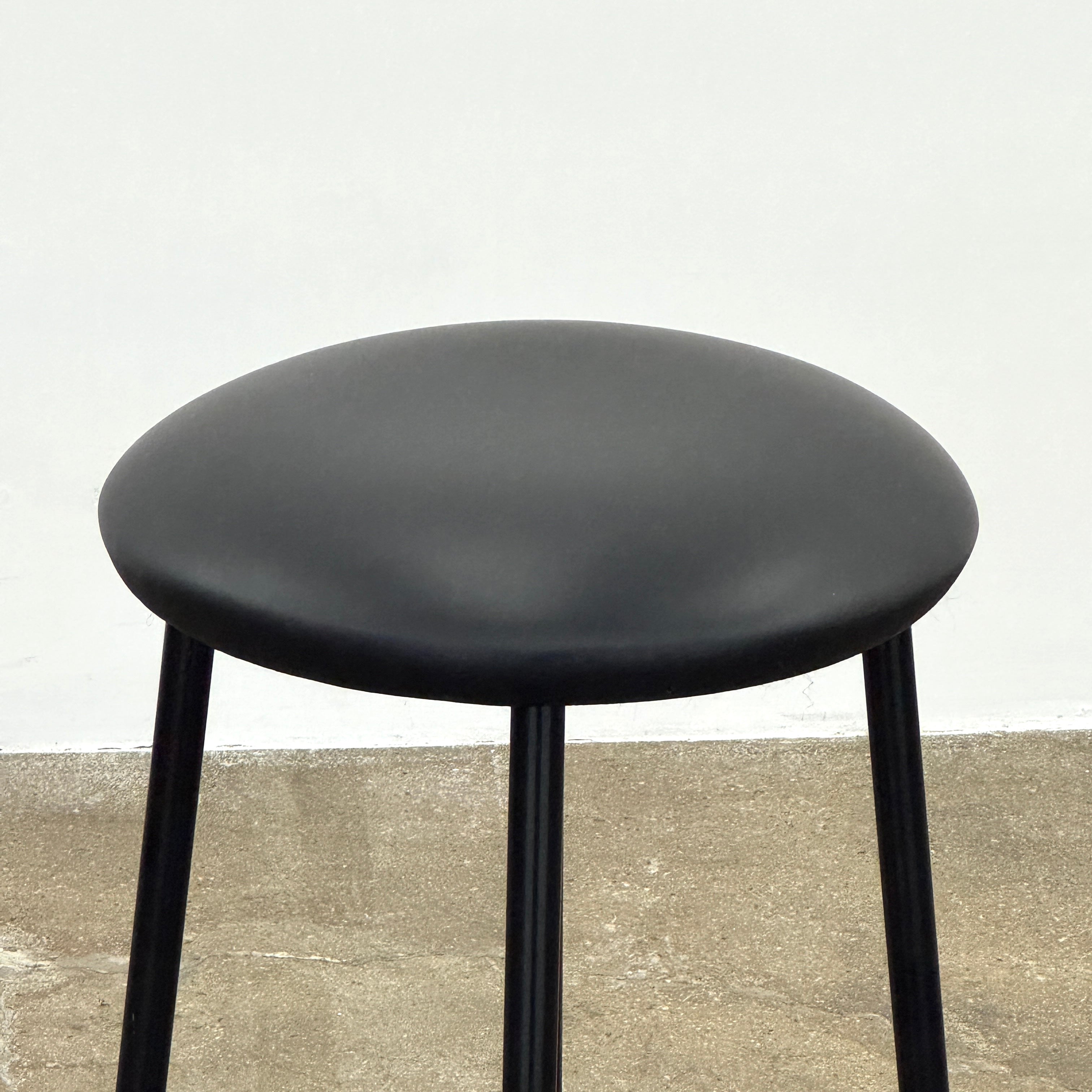 A set of three Johanson Design Sputnik Counter Stools by Modern Resale, featuring round seats and metal legs, are arranged in a row on a concrete floor against a white wall, bringing enduring style to any space.