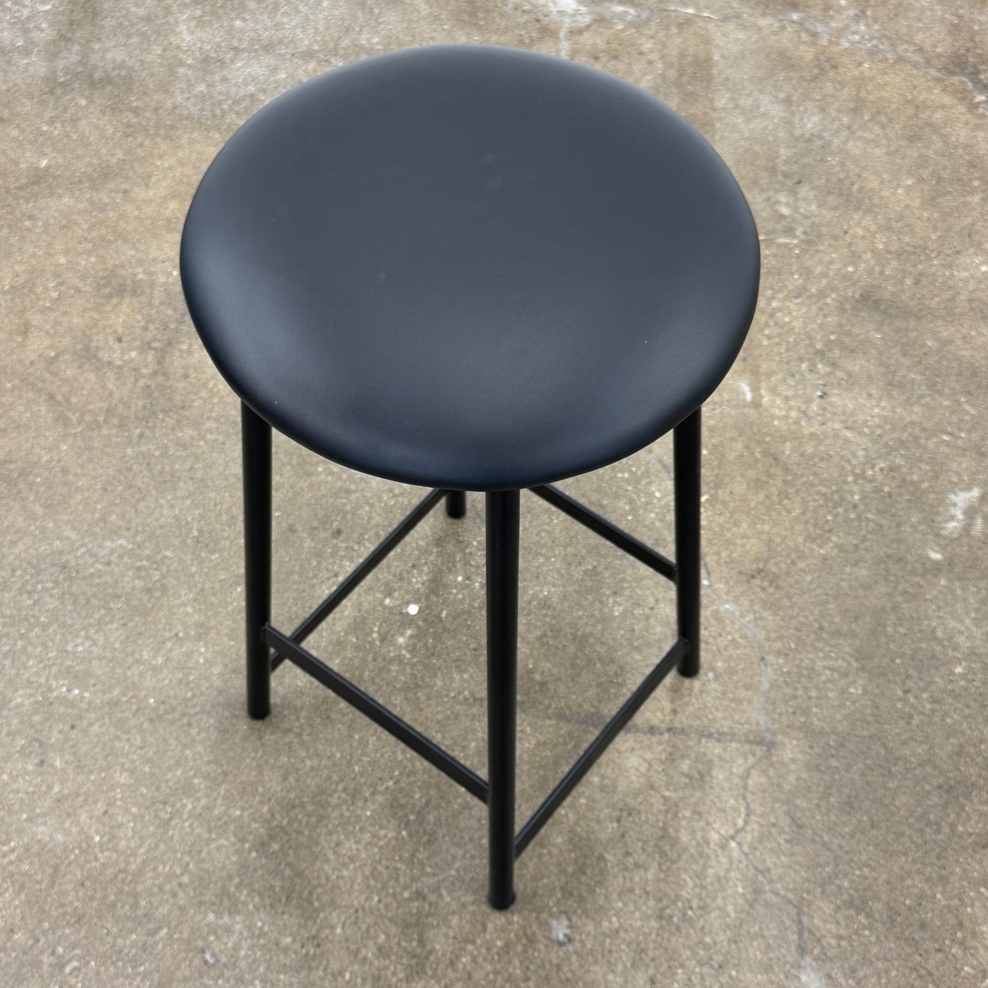 A set of three Johanson Design Sputnik Counter Stools by Modern Resale, featuring round seats and metal legs, are arranged in a row on a concrete floor against a white wall, bringing enduring style to any space.
