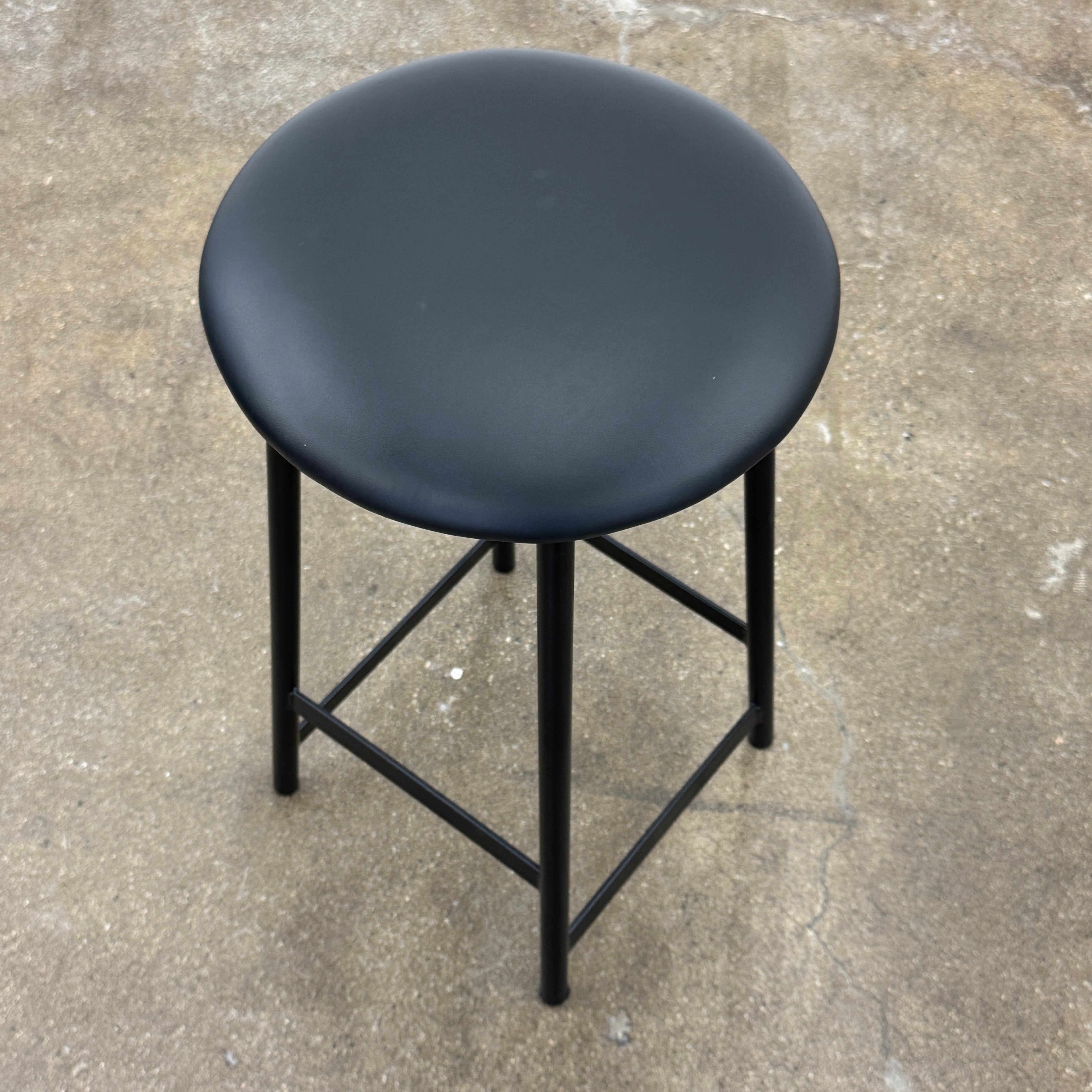 A set of three Johanson Design Sputnik Counter Stools by Modern Resale, featuring round seats and metal legs, are arranged in a row on a concrete floor against a white wall, bringing enduring style to any space.