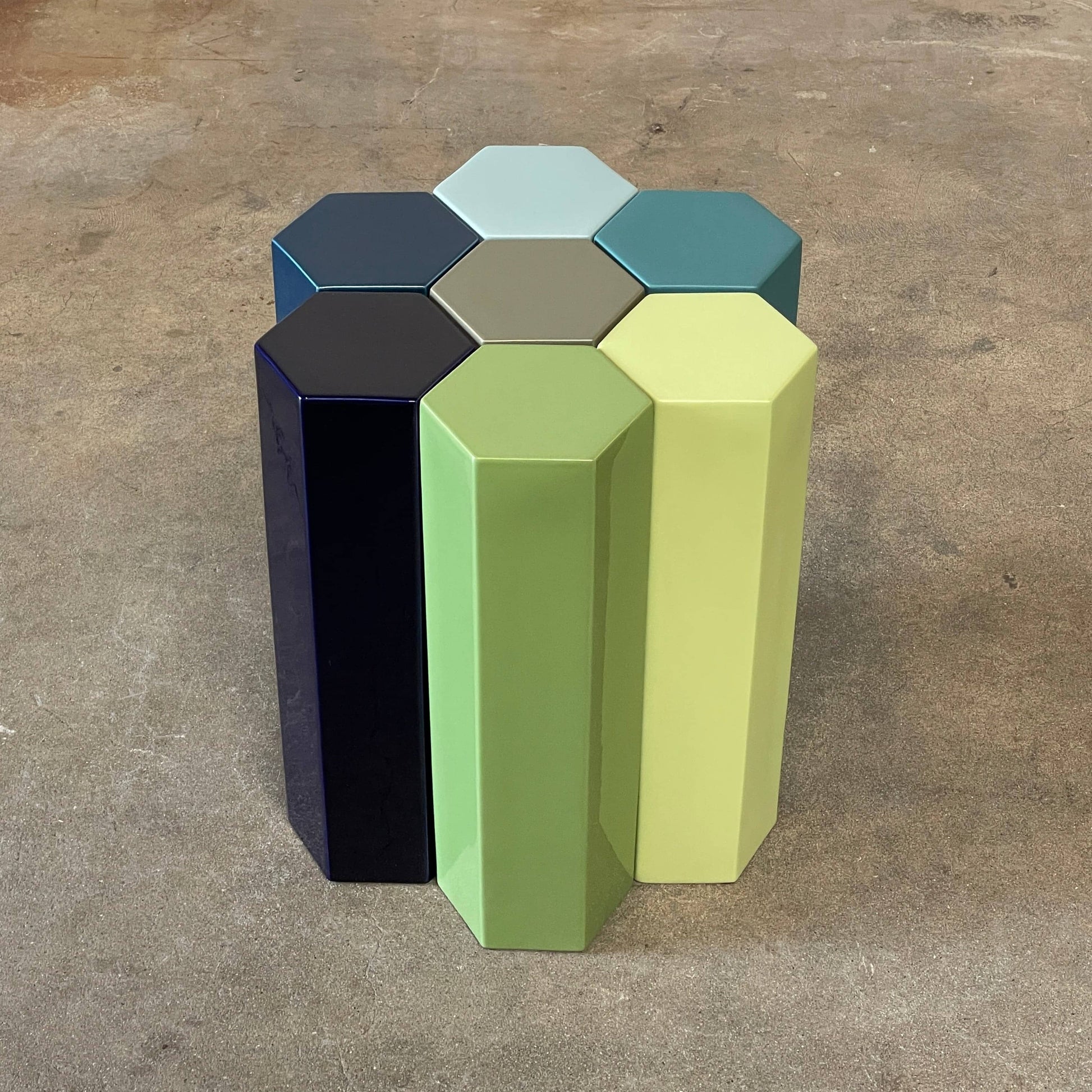 The Delcourt Collection MUC 7 Side Tables feature interconnected ceramic hexagons in green, blue, brown, and gray on a light gray background. Echoing Christophe Delcourt's design ethos, these versatile pieces enhance any space with style and functionality.