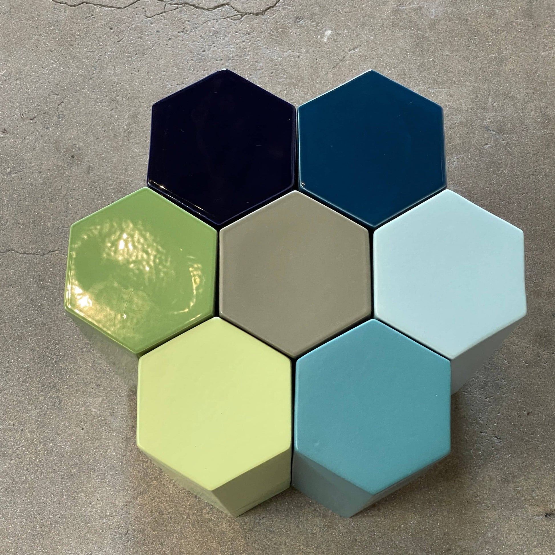 The Delcourt Collection MUC 7 Side Tables feature interconnected ceramic hexagons in green, blue, brown, and gray on a light gray background. Echoing Christophe Delcourt's design ethos, these versatile pieces enhance any space with style and functionality.