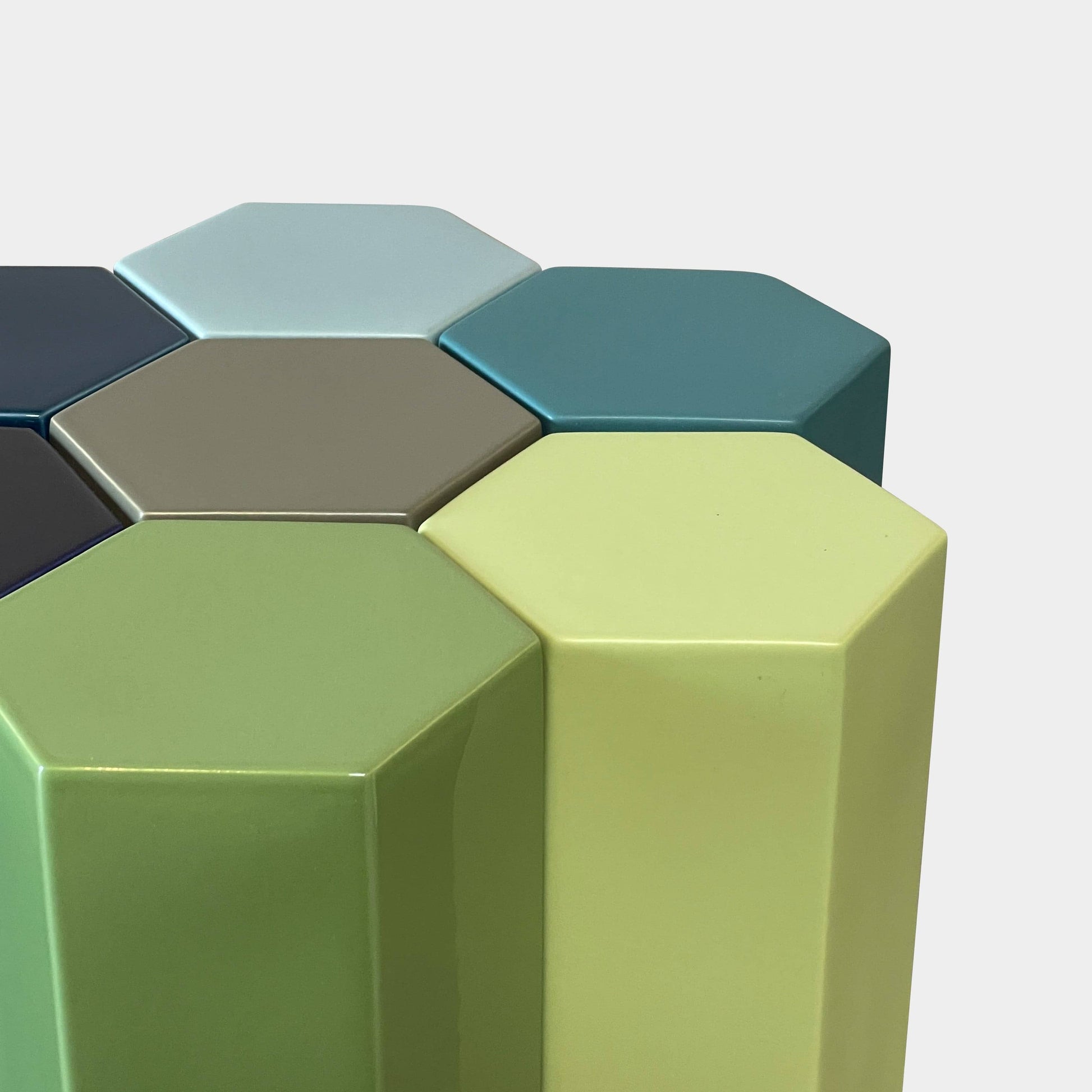 The Delcourt Collection MUC 7 Side Tables feature interconnected ceramic hexagons in green, blue, brown, and gray on a light gray background. Echoing Christophe Delcourt's design ethos, these versatile pieces enhance any space with style and functionality.
