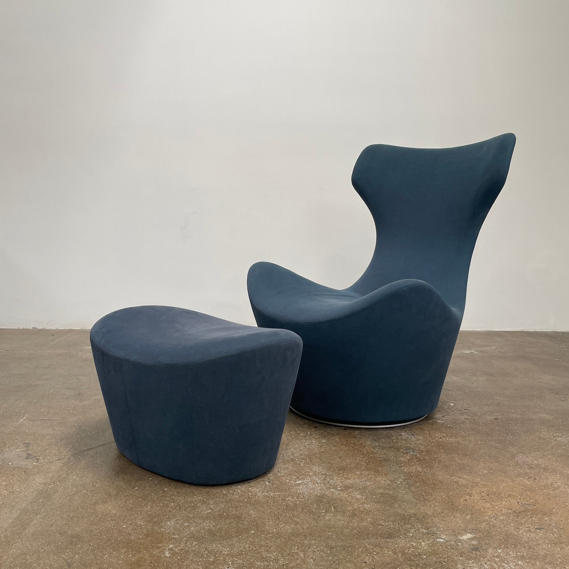 The B&B Italia Grande Papilio Swivel Chair with Ottoman features a modern design inspired by Naoto Fukasawa, with a dark blue finish, wide seat, curved armrests, and a high winged backrest—a signature piece from B&B Italia.