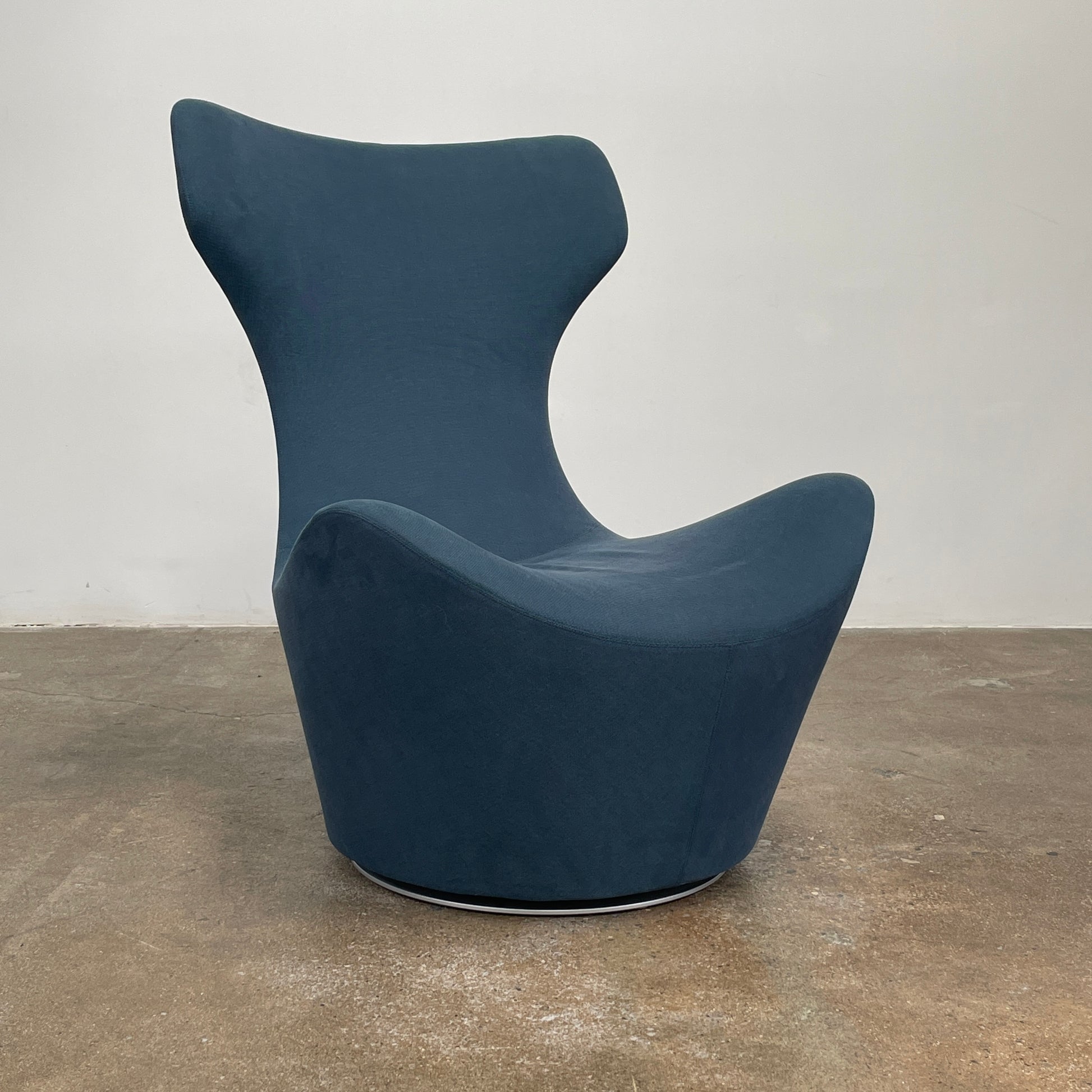The B&B Italia Grande Papilio Swivel Chair with Ottoman features a modern design inspired by Naoto Fukasawa, with a dark blue finish, wide seat, curved armrests, and a high winged backrest—a signature piece from B&B Italia.